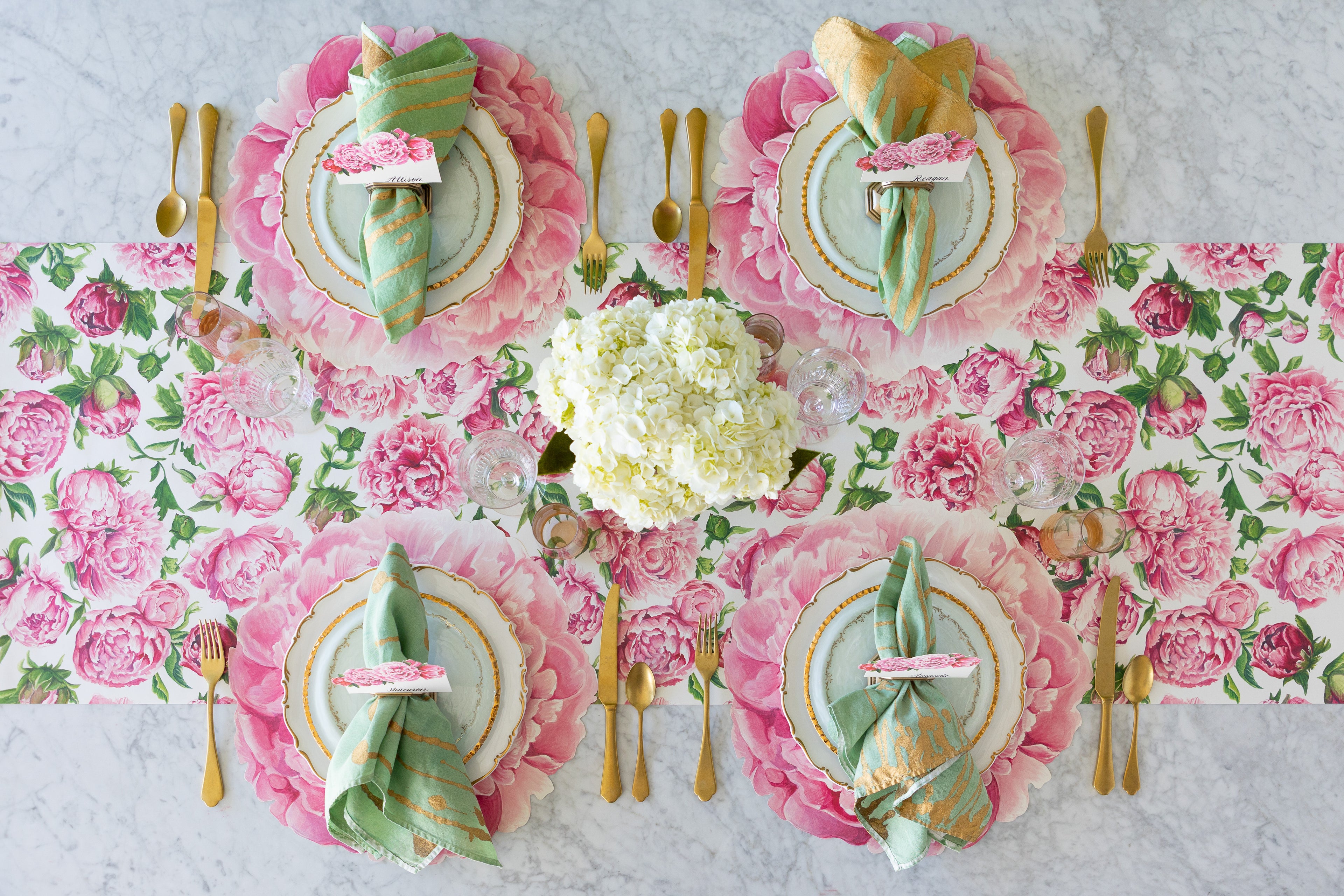 A decorative table setting with the Peonies in Bloom Runner, Die-cut Peony Placemats, decorative plates, Peonies Place Cards, marbled napkins and gold flatware.
