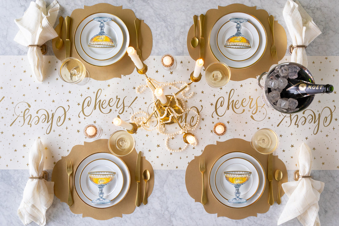 Elegant table setting with gold and white decor, including plates, glasses, and a bottle.