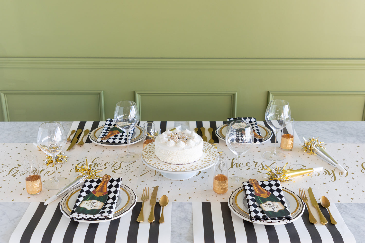 Dining table set with a cake, plates, and cutlery on a striped tablecloth against a green wall.