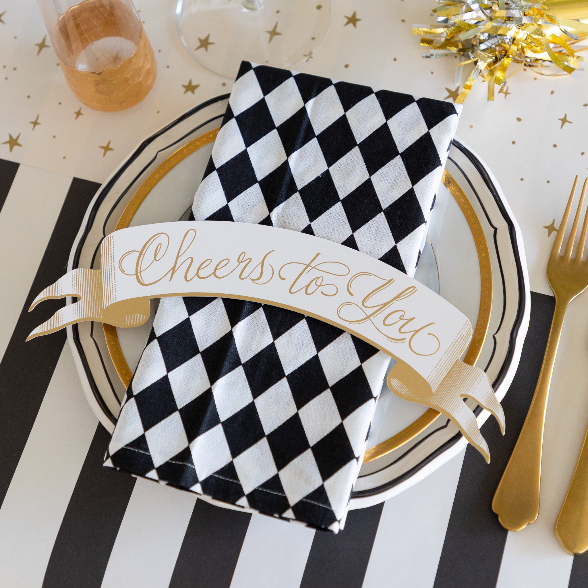 Decorative table setting with black and white checkered napkin, gold cutlery, and &