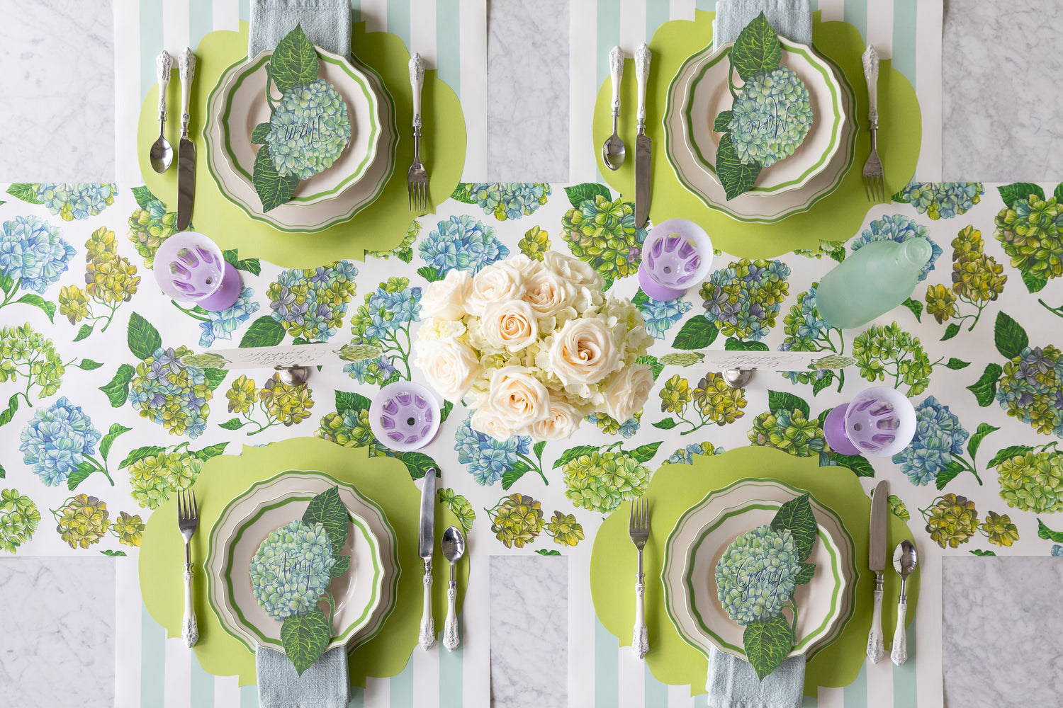 An elegant table set with flowers, Die-cut Bright Green French Frame Placemats, Hydrangea Table Accents, Green Icing on the Cake Dinnerware and purple glasses on the Hydrangea Runner.