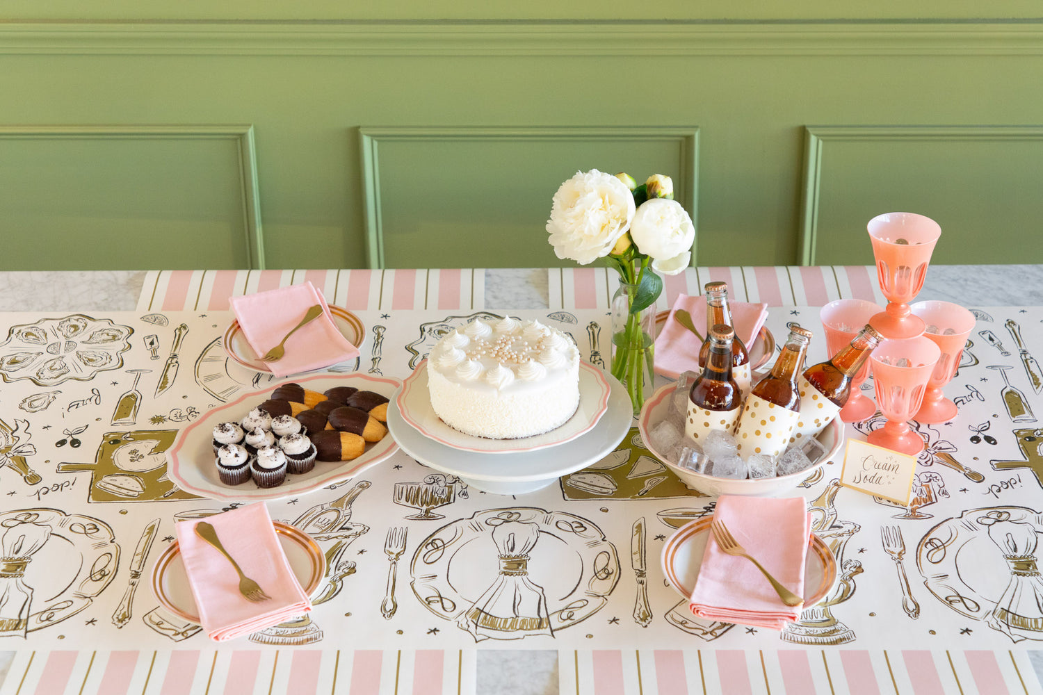 Dining table set with a cake, cookies, and drinks on a patterned table runner.