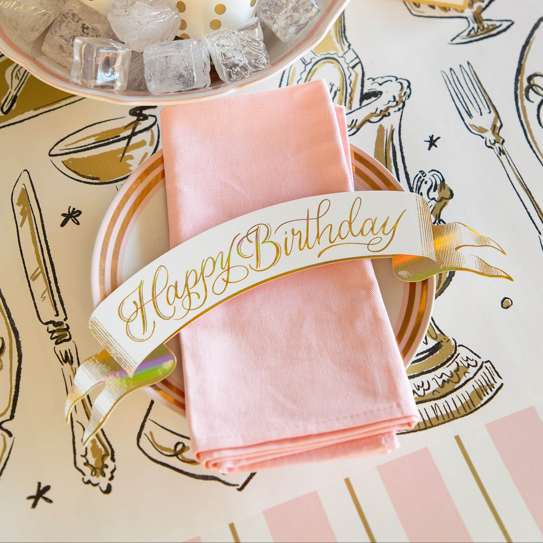 Decorative table setting with the Happy Birthday Banner table accent on a pink napkin and plate with the Cocktail Party Runner underneath.