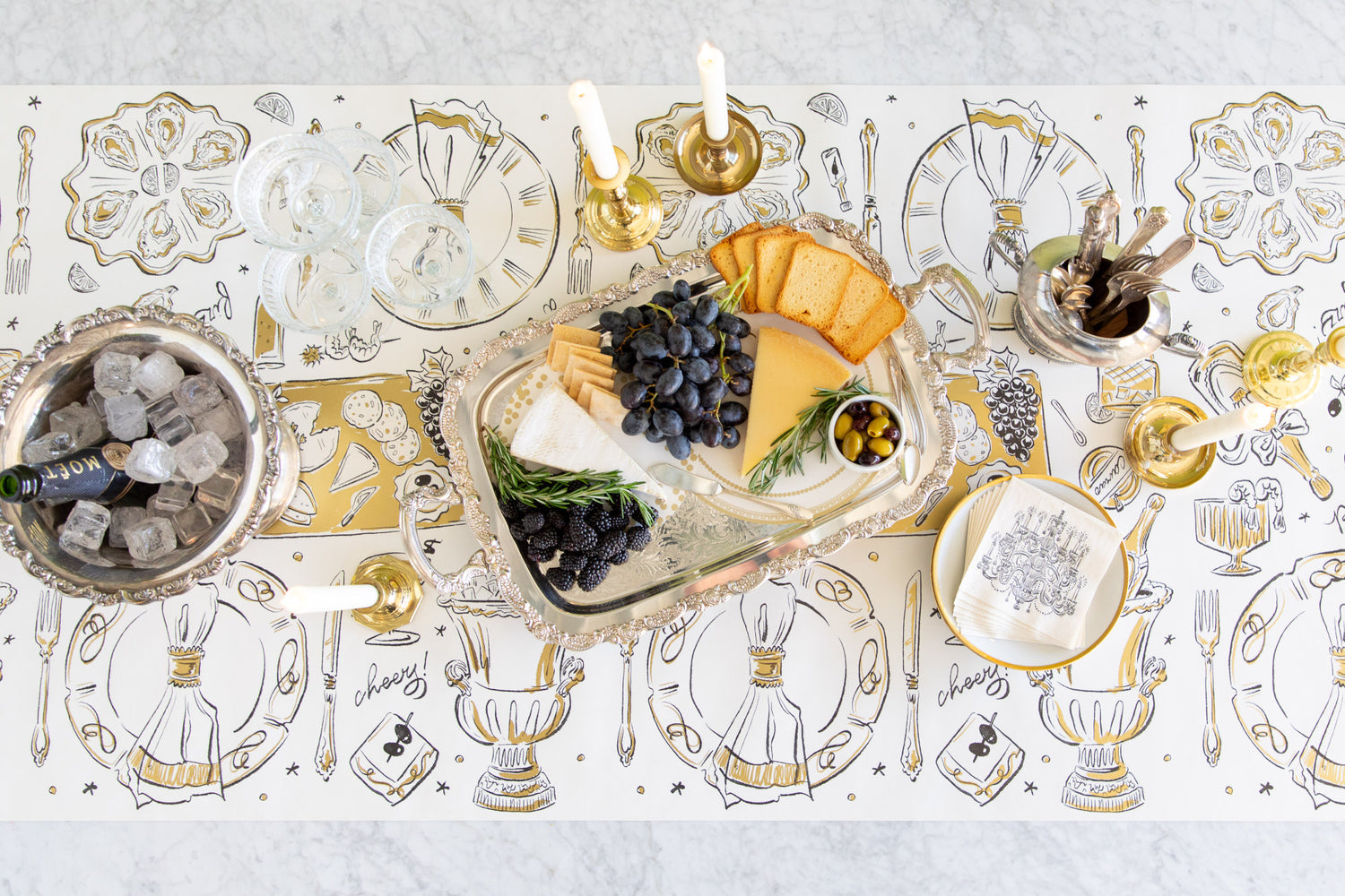 Table Runner with hand drawn illustrations of party tabletop items with a bucket of champagne, candle holders and a charcuterie tray set upon it. 