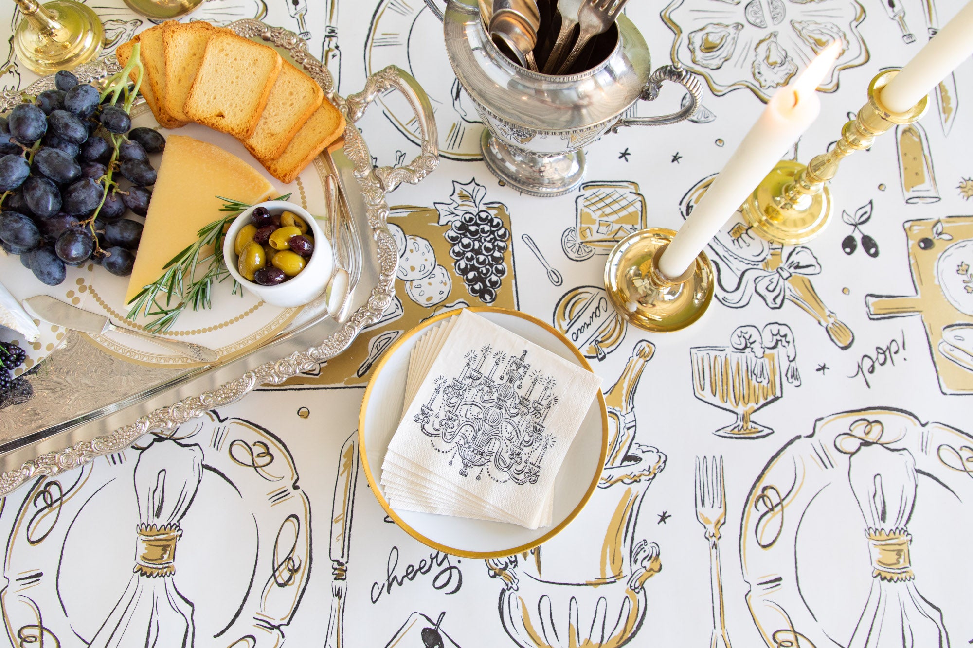 Table setting with cheeseboard, grapes, and cutlery on a decorative tablecloth.