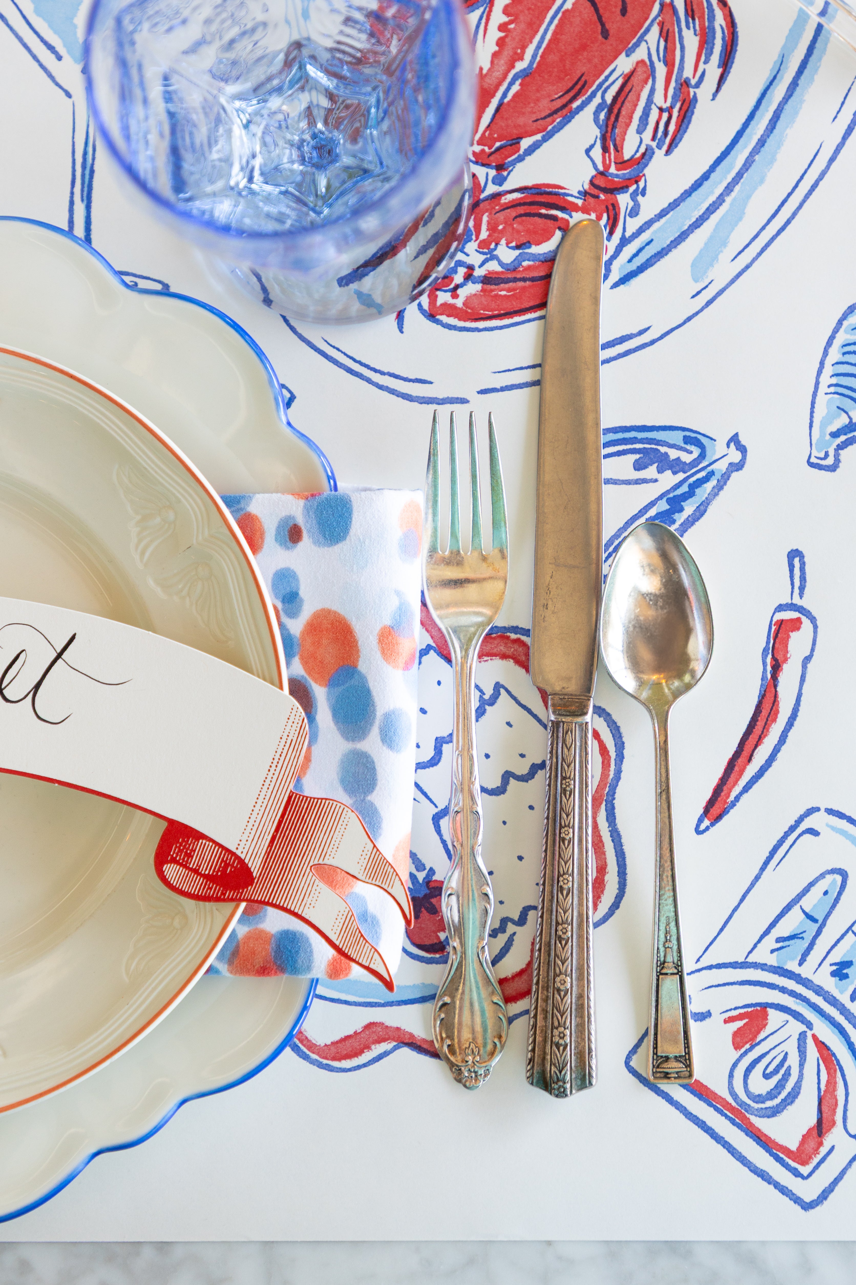 Dinner setting with colorful table runner, plate, and cutlery on a marble surface.