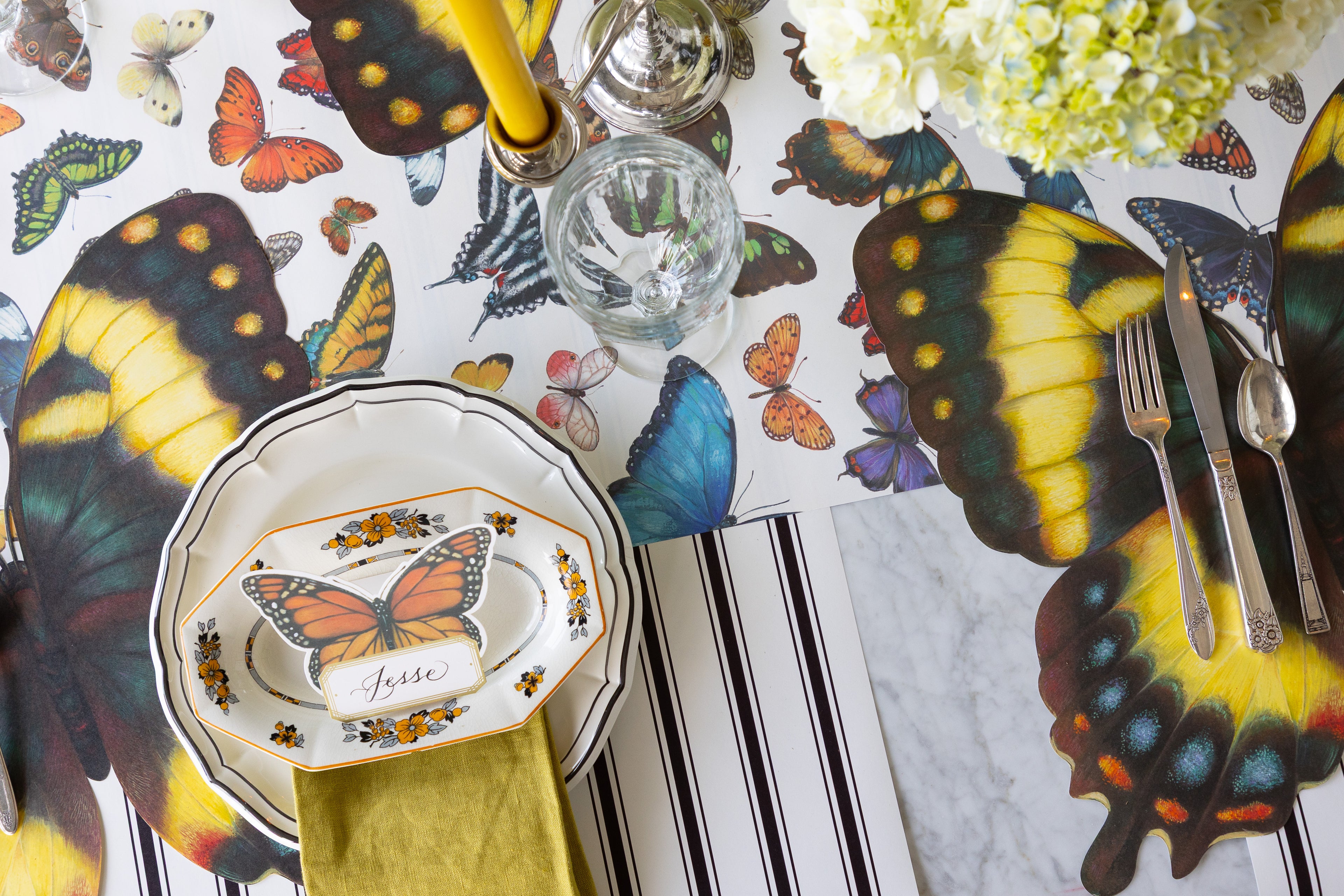 Butterfly-themed table setting with flowers, candles, Die-cut Butterfly Placemats, Butterfly Place Card and Black Icing on  the Cake plates on the Butterflies and Black Linen Stripe Runners.