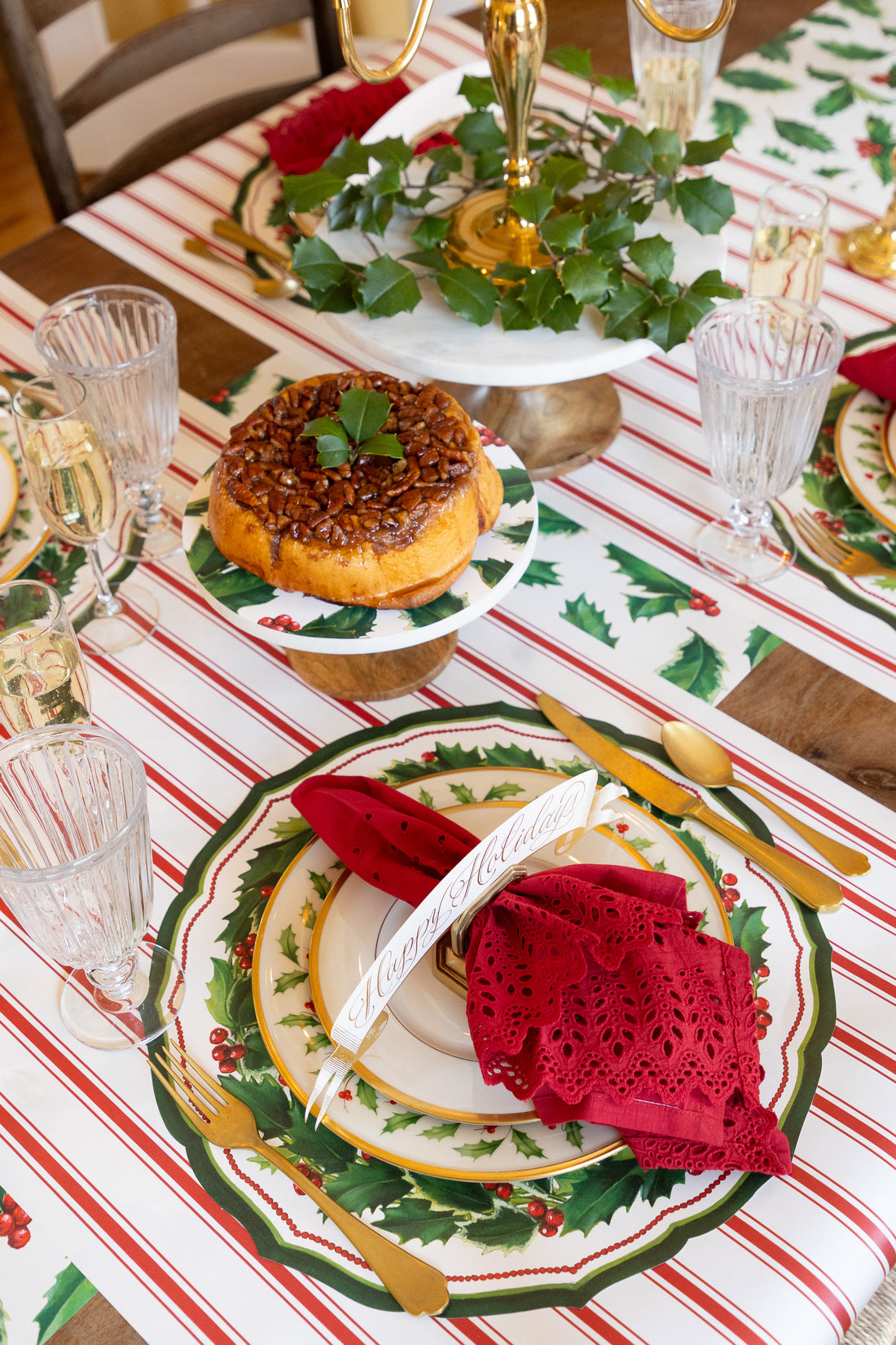 Holiday table setting with the Die-cut Holiday Holly China Placemat, with red napkin, table card and gold cutlery. 