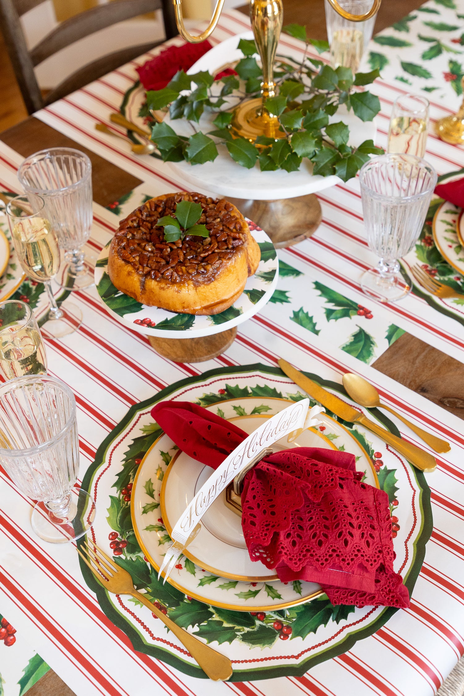 Holiday table setting with the Die-cut Holiday Holly China Placemat, with red napkin, table card and gold cutlery. 