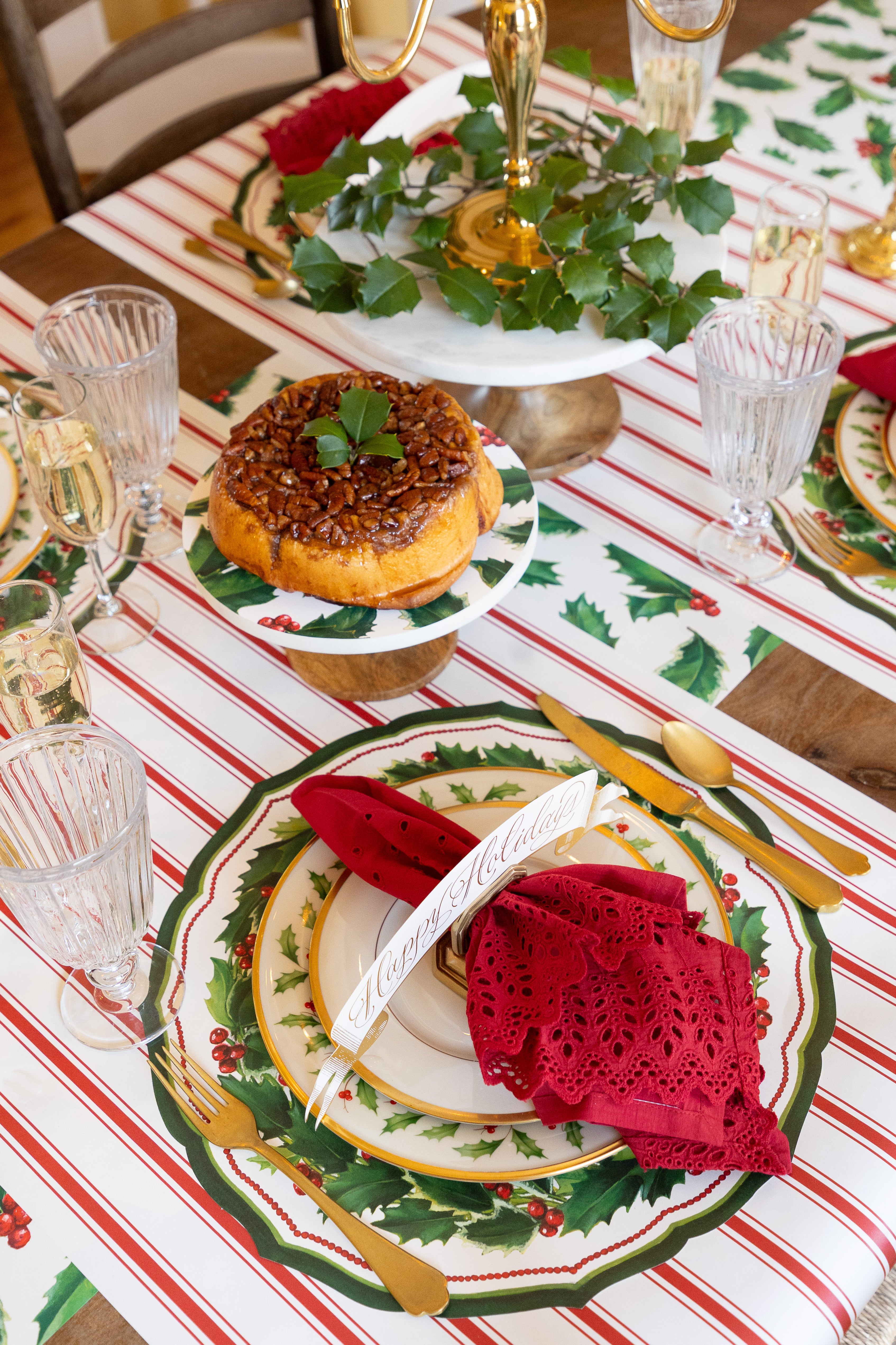 Holiday table setting with the Die-cut Holiday Holly China Placemat, with red napkin, table card and gold cutlery. 