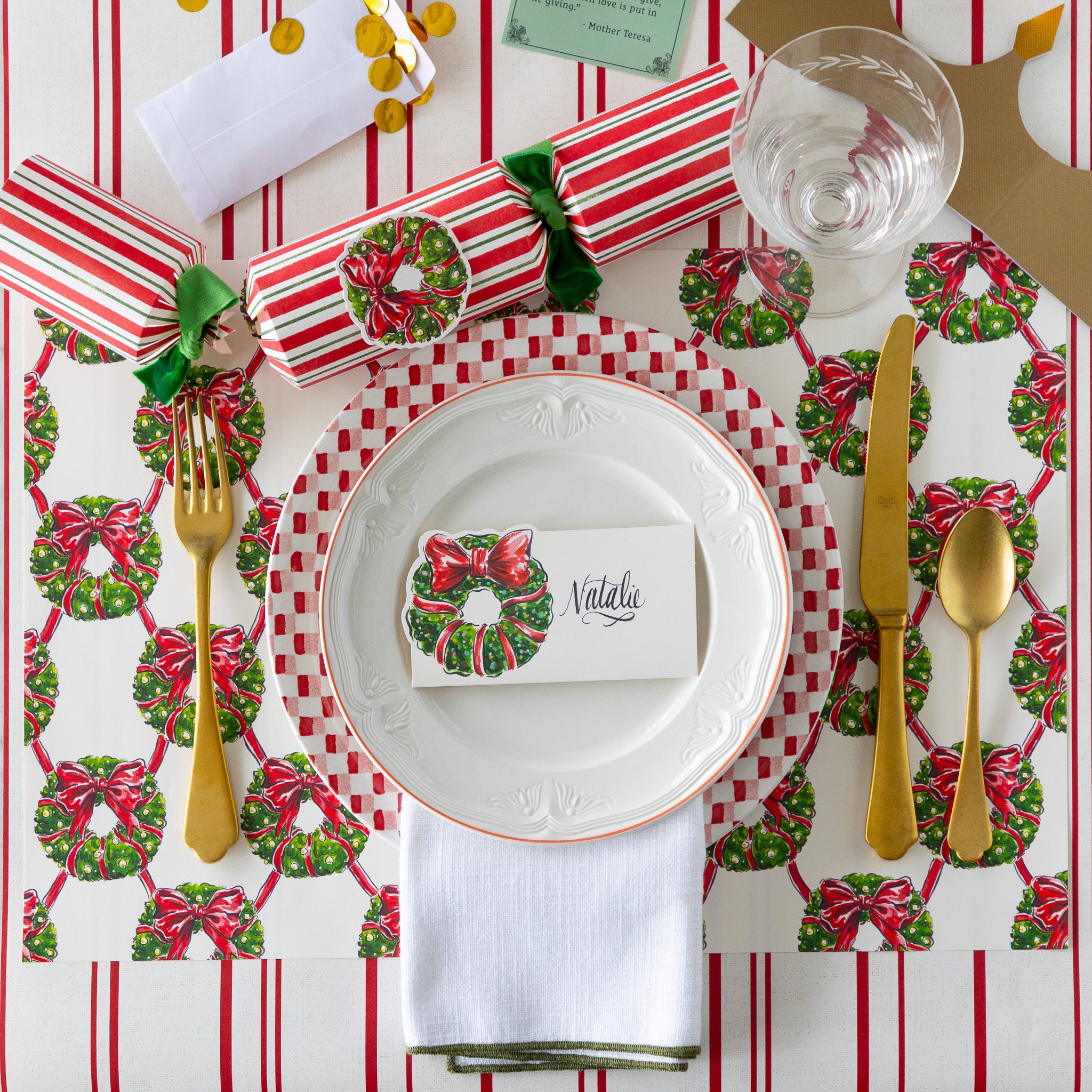 A festive place setting featuring the Holiday Wreath Lattice Placemat, Holiday Wreath Place Card, an opened Holiday Wreath Festive Cracker and gold flatware on the Antique Red Striped Runner.
