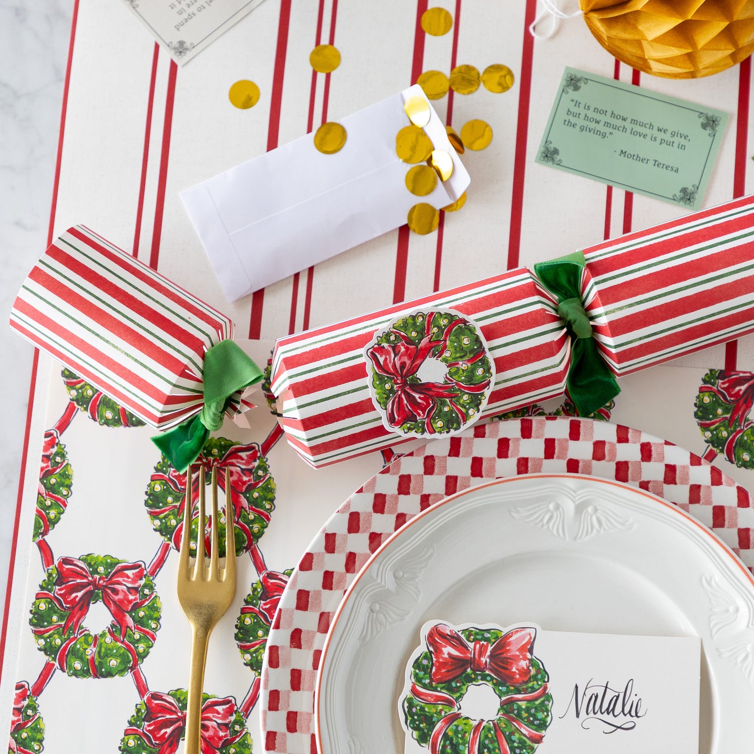 A Christmas table setting featuring the Holiday Wreath Placemats, Holiday Wreath Crackers partially opened with their contents on the table, and Red Awning Stripe Runner underneath.