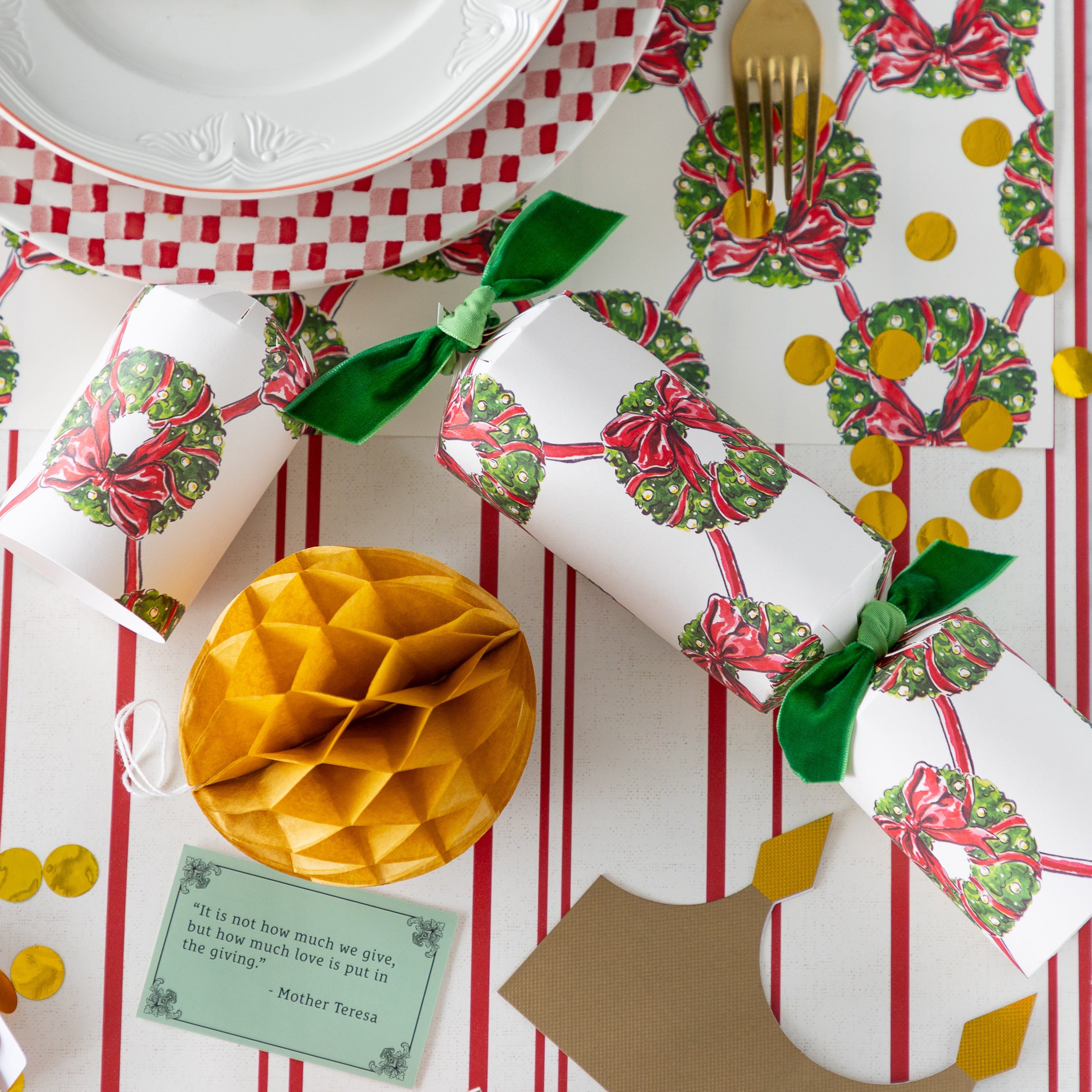 A table setting with the Holiday Wreath Cracker opened with its contents–– a gold honeycomb ball, crown, confetti, and a question––on the table.