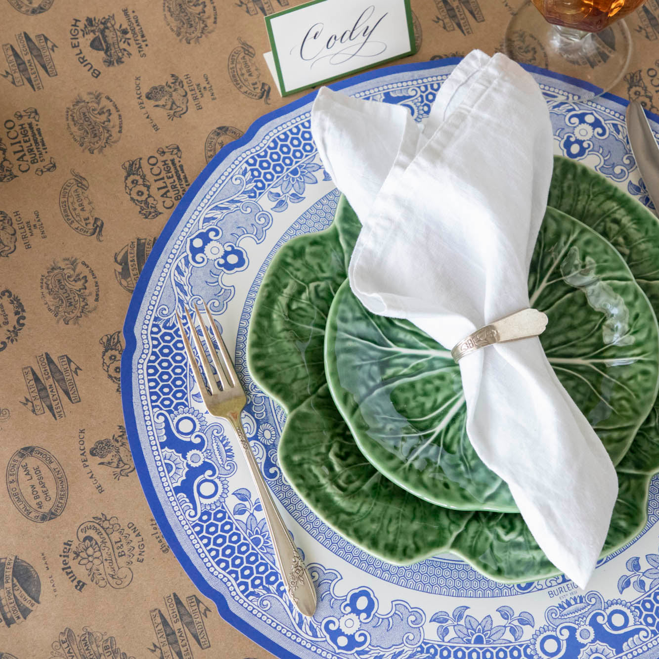 Die-cut Blue Willow Plate Placemat with an elegant place setting on top and Kraft Burleigh Heritage Runner underneath.