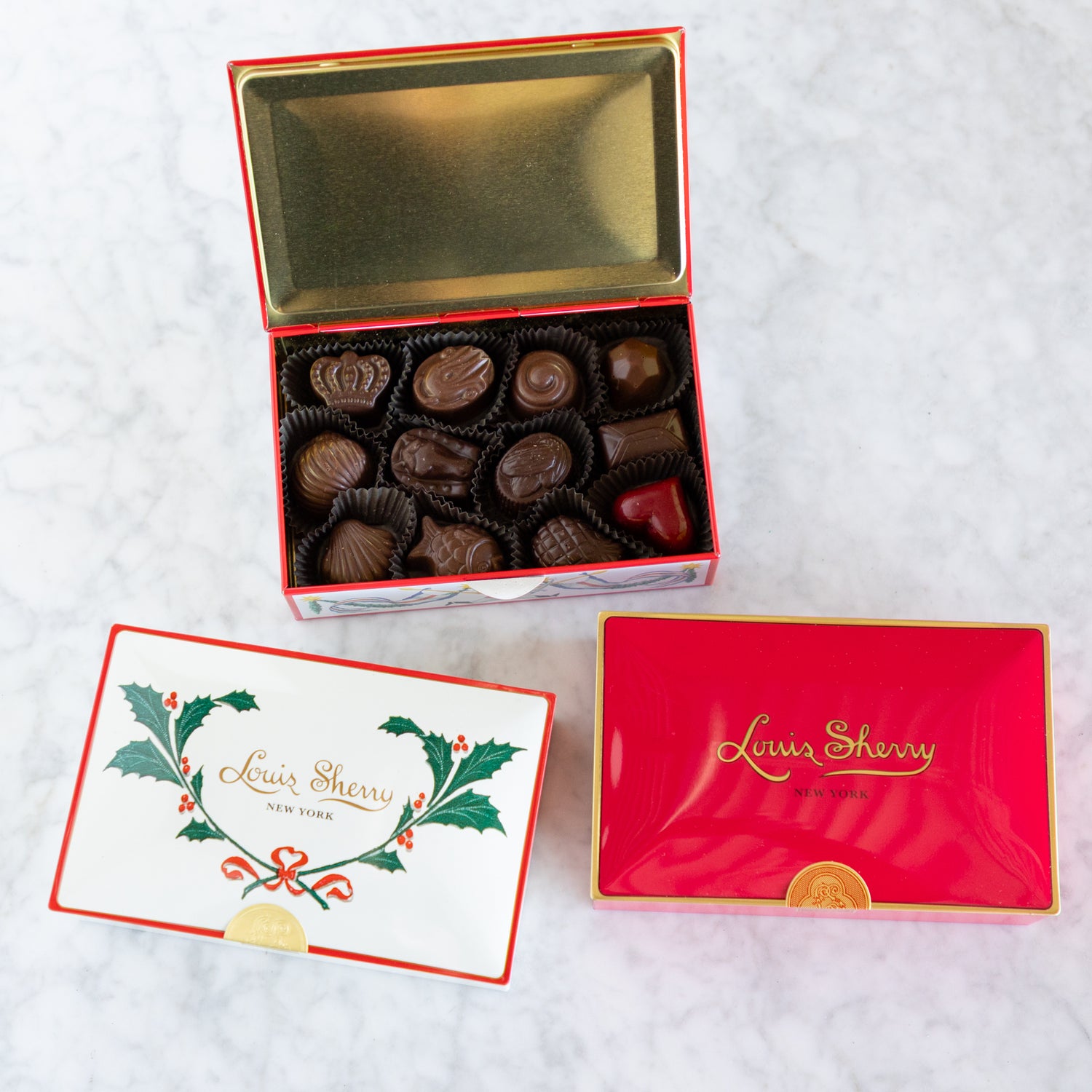 Open box of chocolates with a card and another closed box on a white background, featuring &