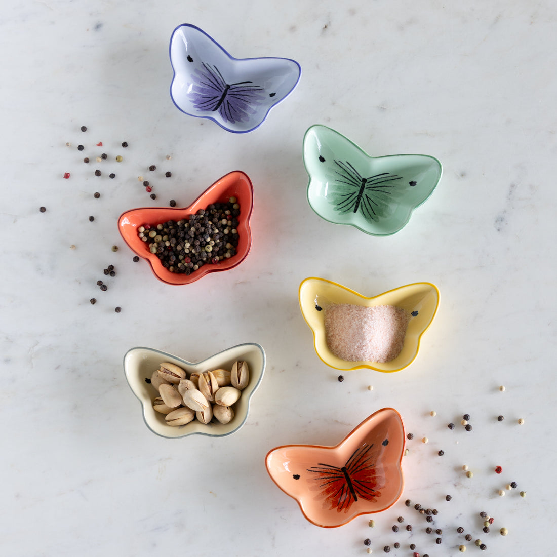 Set of colorful butterfly-shaped ceramic bowls on a marble surface with spices.