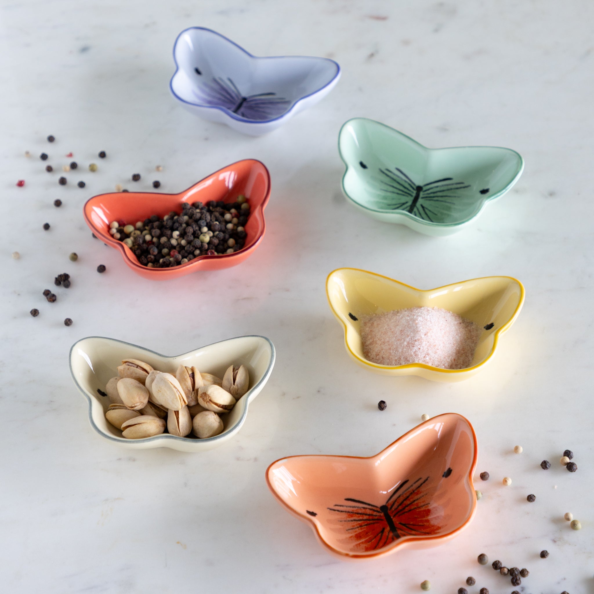 Set of colorful butterfly-shaped ceramic bowls on a light surface with various contents.