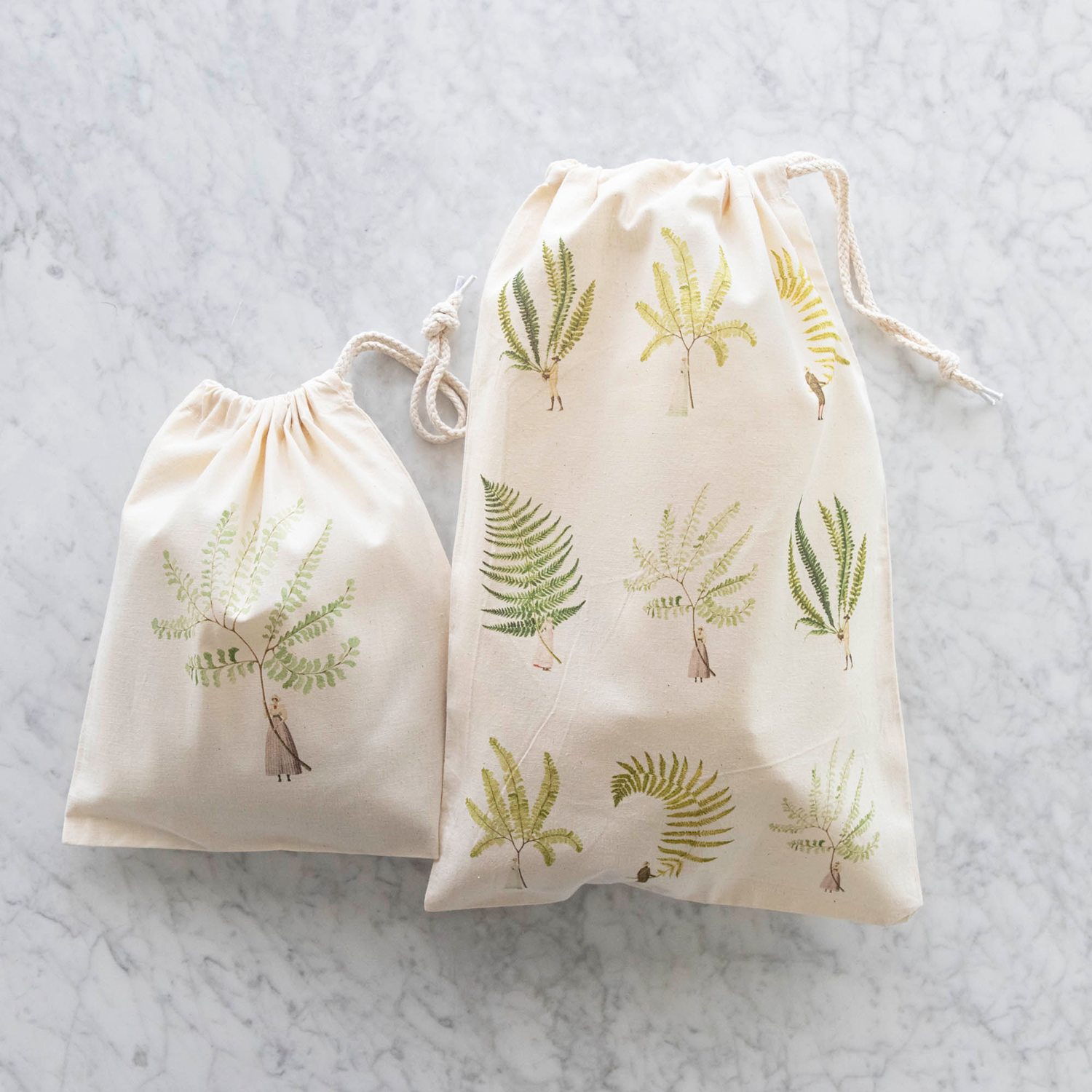 wo of the Laura Stoddart Drawstring Bags - the Small Fern 2 Bag and the Medium Fabulous Ferns Bag, both resting on a white table. 