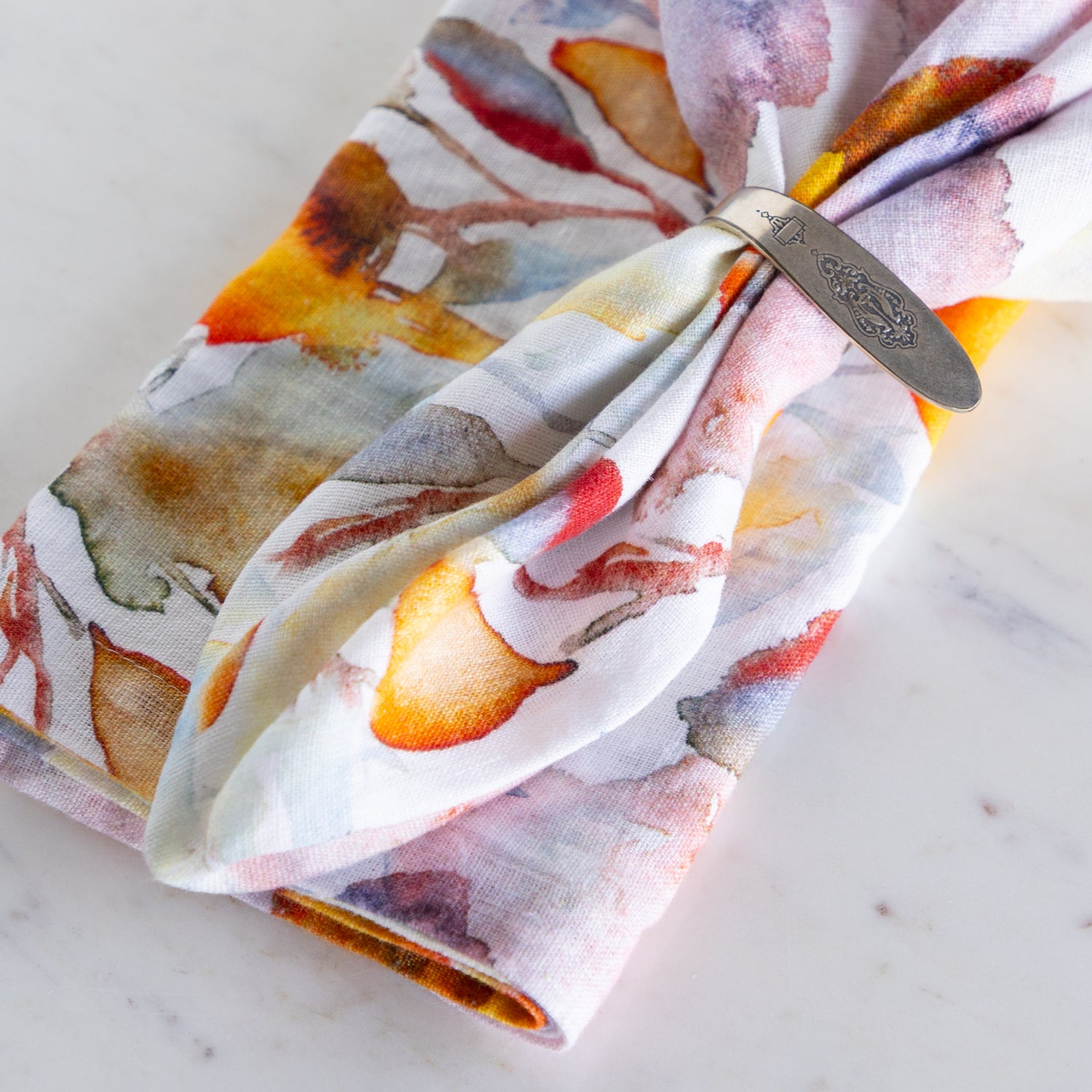 Folded napkin with a floral pattern and a metal napkin ring on a marble surface.