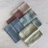 Set of five folded napkins in various earthy tones on a light marble surface.