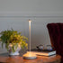 A Sand LED Cordless Lamp by Zafferano on a table next to a book and a plant.