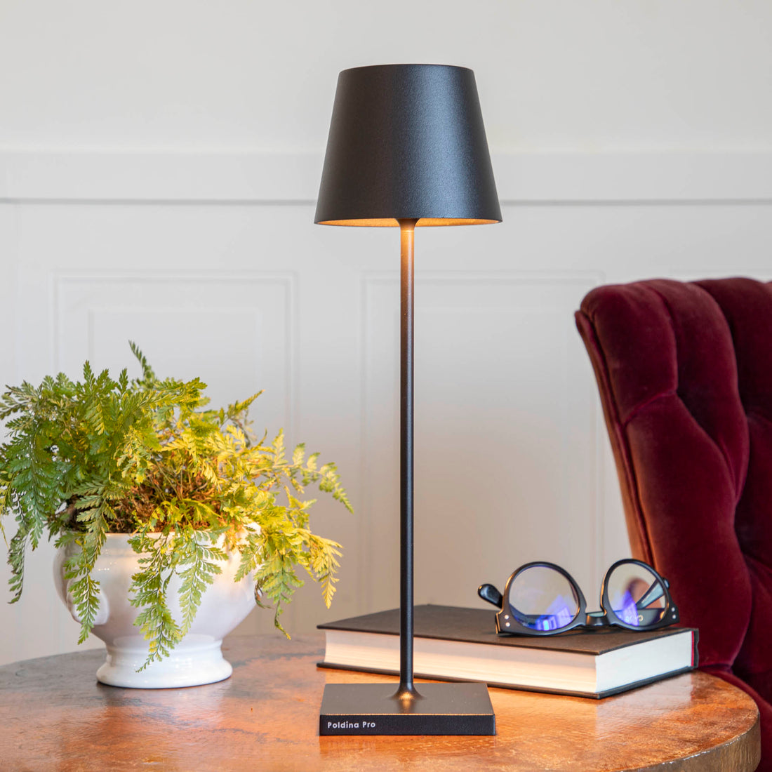 A Black Cordless Lamp by Zafferano on a table next to a book and a plant.
