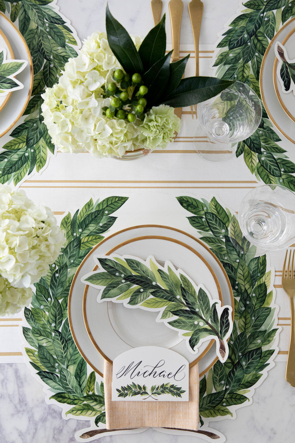 A table setting with Die-cut Green Laurel Wreath Placemats from Hester &amp; Cook and gold plates.