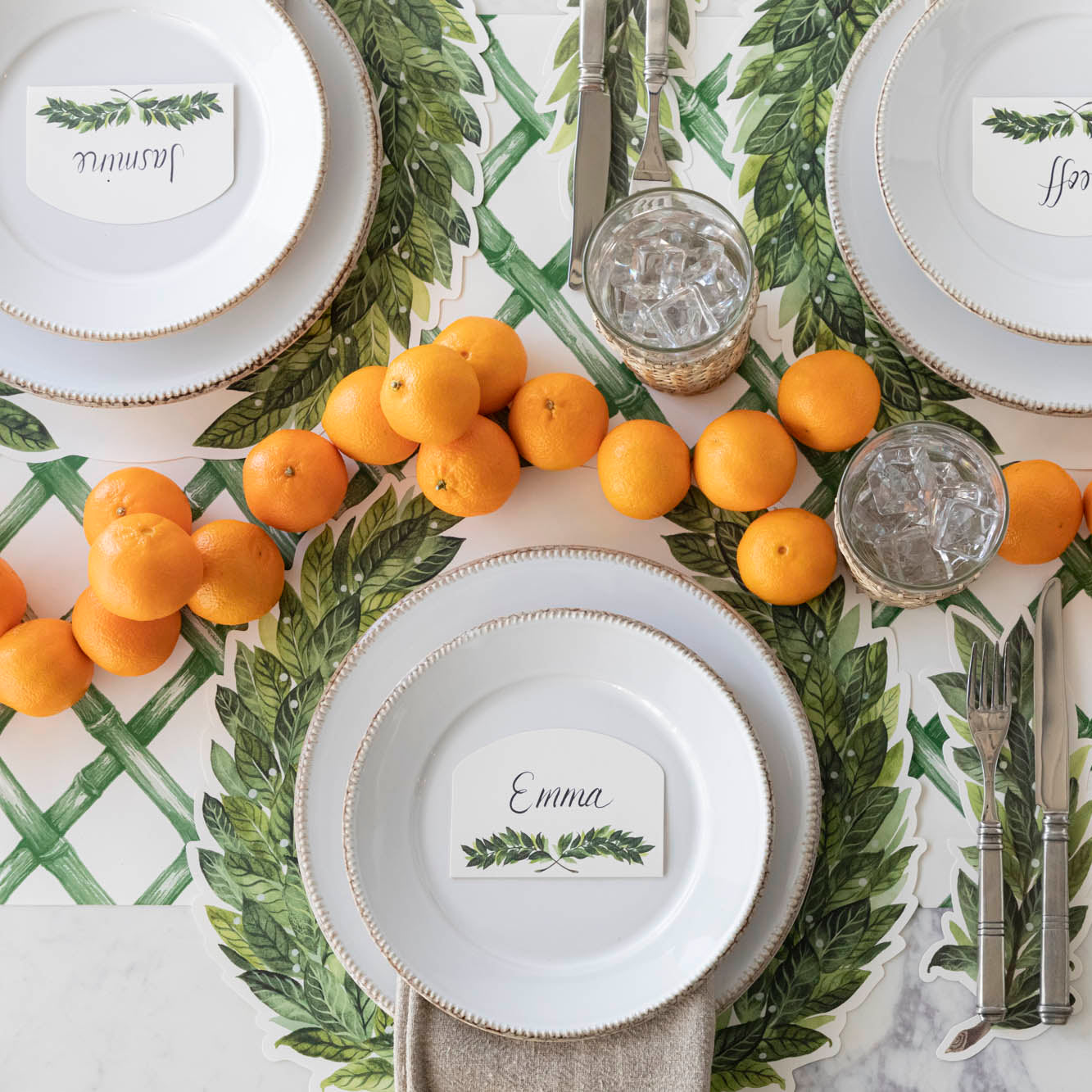 Die-cut Laurel Placemat on the Green Lattice Runner on a place setting for three, with oranges arranged down the center of the table.