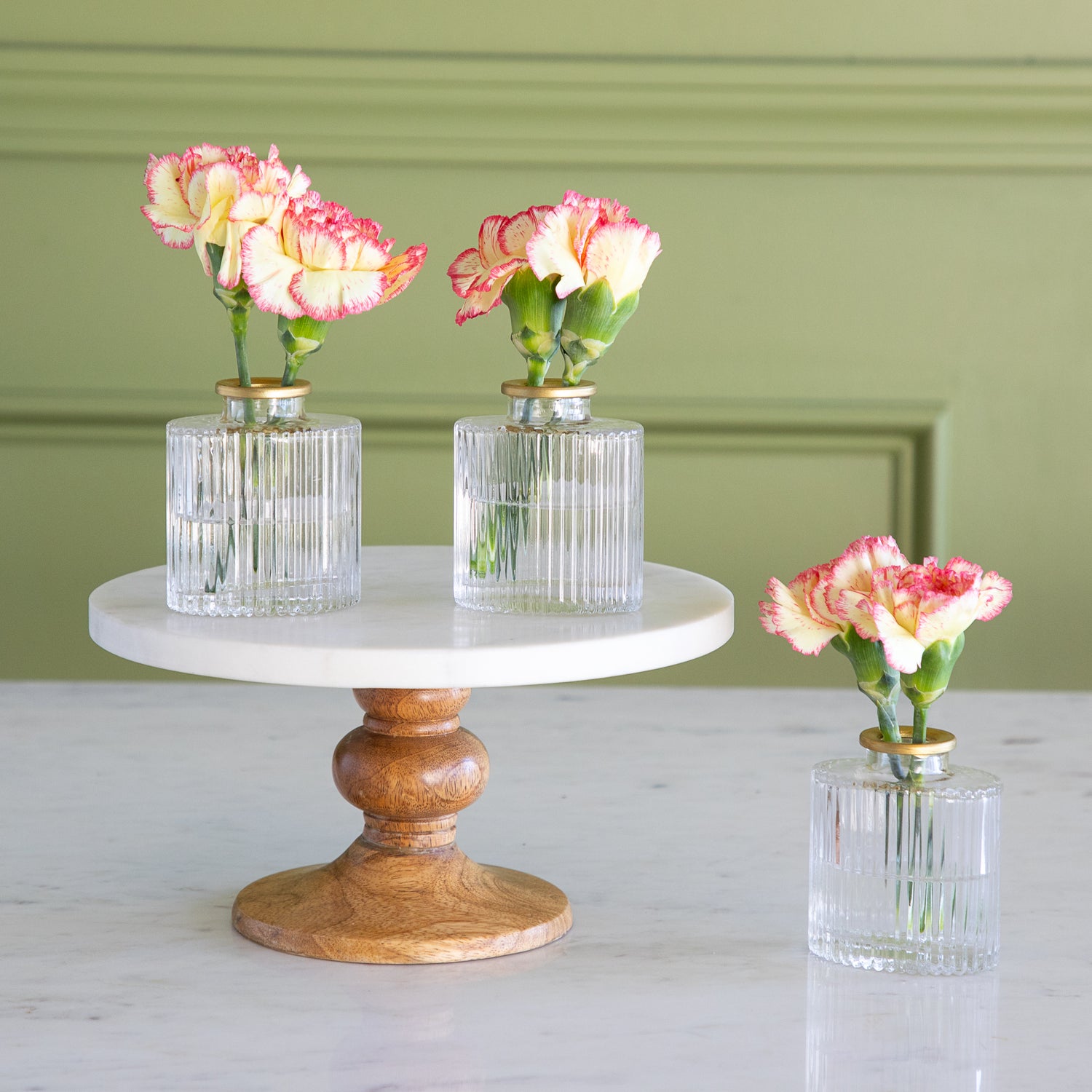 Three small vases with flowers on a marble and wood stand against a green wall.
