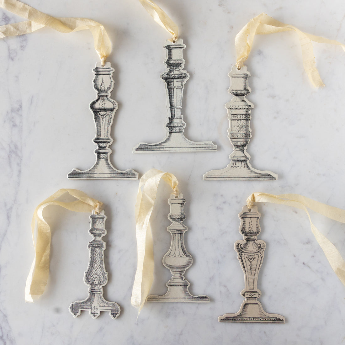 Decorative silver candlestick ornaments with ribbons on a marble surface.