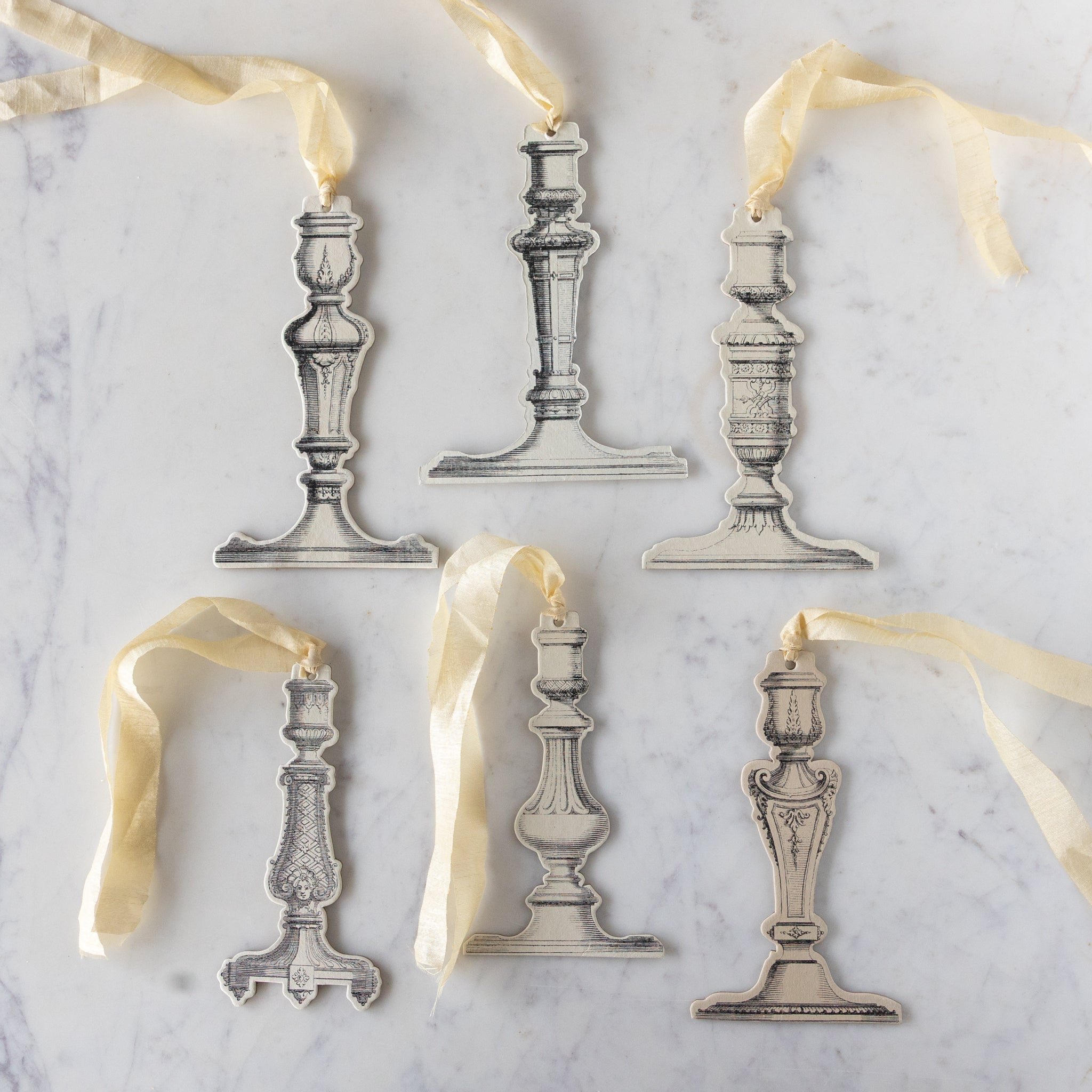 Decorative silver candlestick ornaments with ribbons on a marble surface.