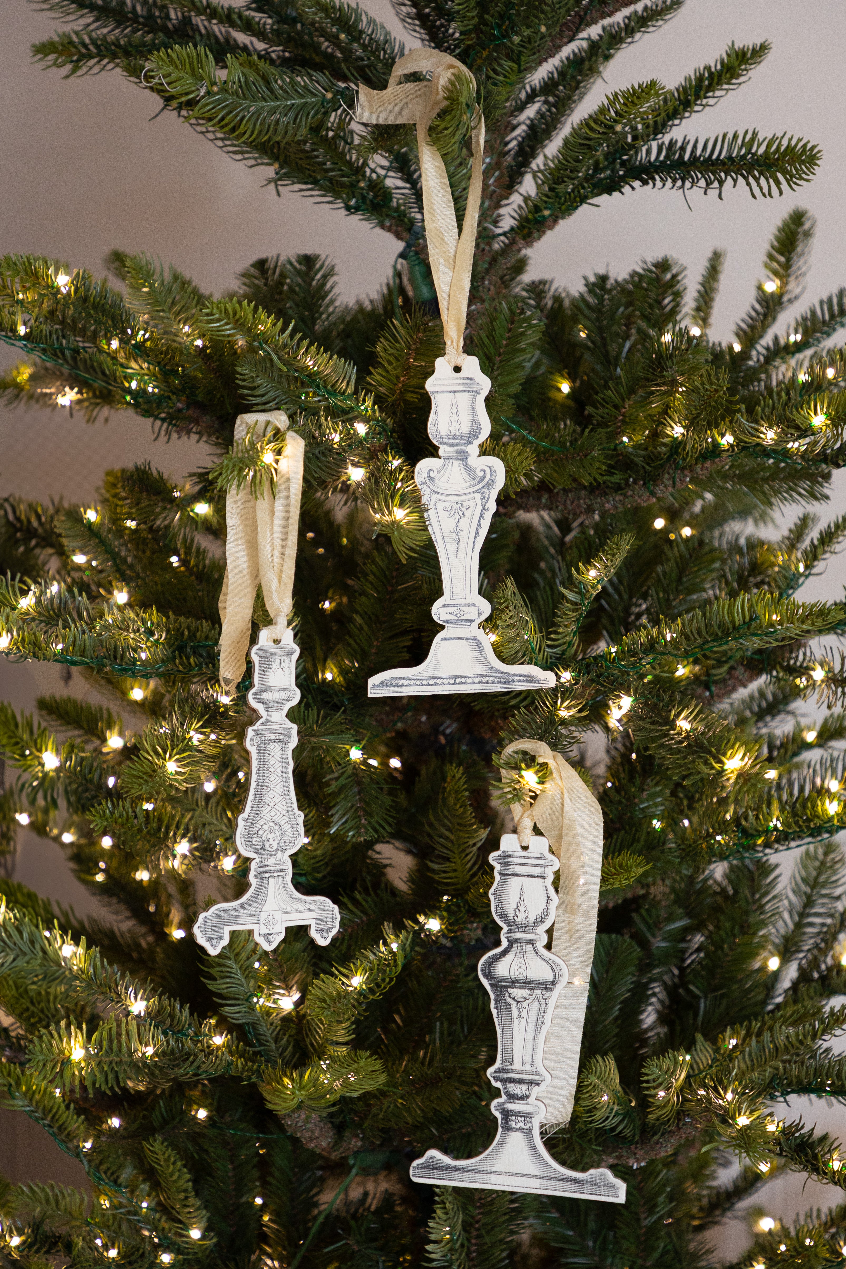 Decorative candlestick ornaments hanging on a Christmas tree with lights.
