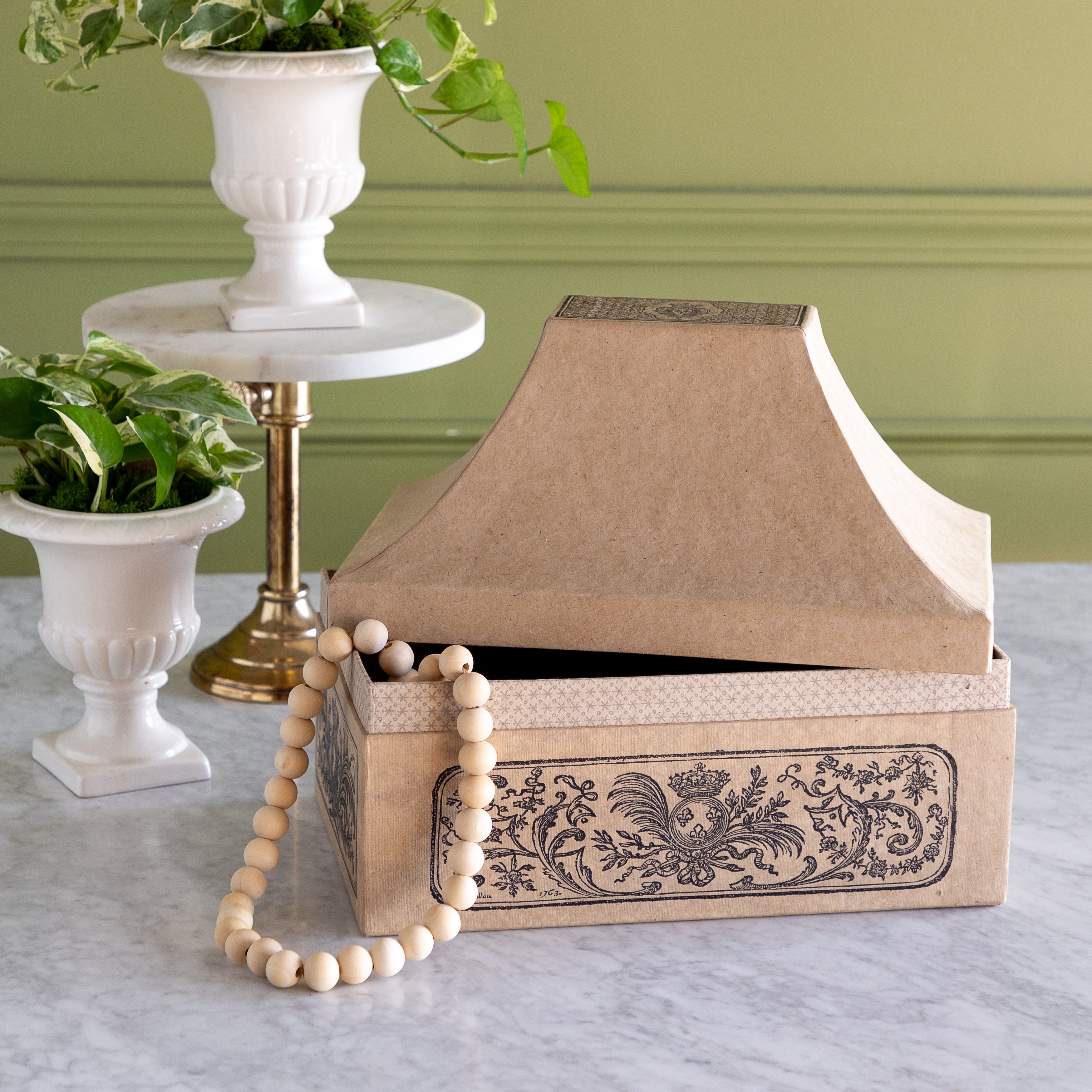 Decorative box with intricate design, beads hanging out, and plant pots on a marble surface.