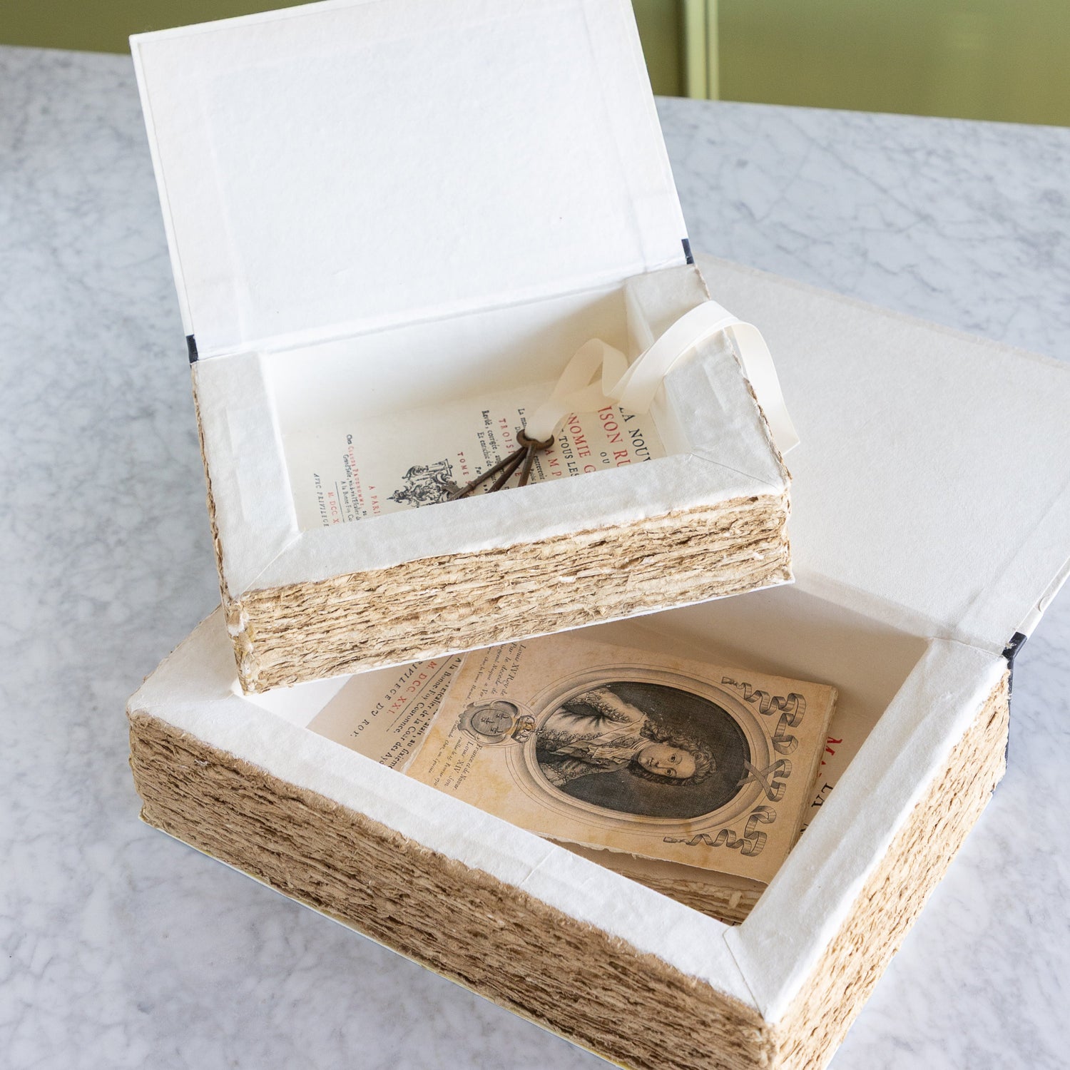 Two open storage boxes with a vintage book inside one and vintage keys in the other.