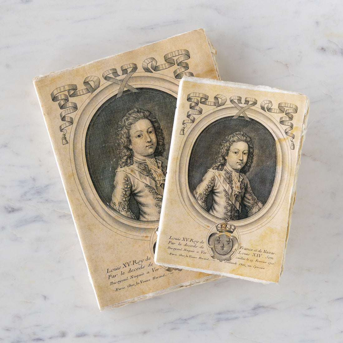 Two vintage notebooks with portraits of Louis XV on a marble surface