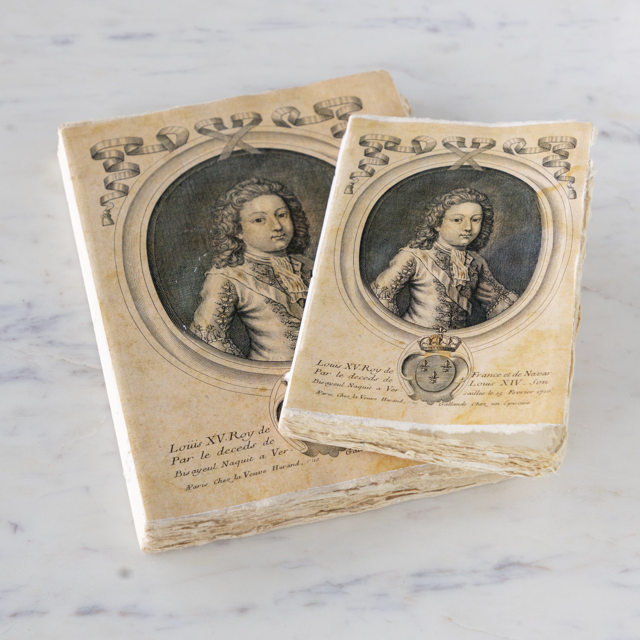Two vintage notebooks with portraits of Louis XV on a marble surface