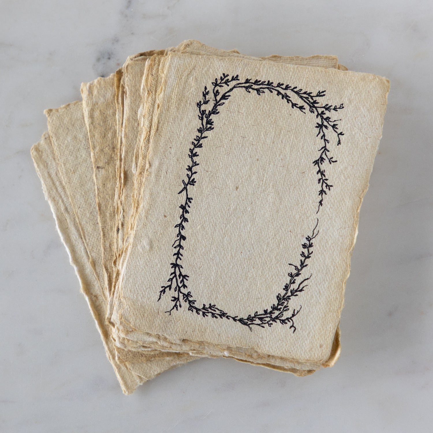 Stack of vintage-style cards with decorative leaf design on a marble surface.