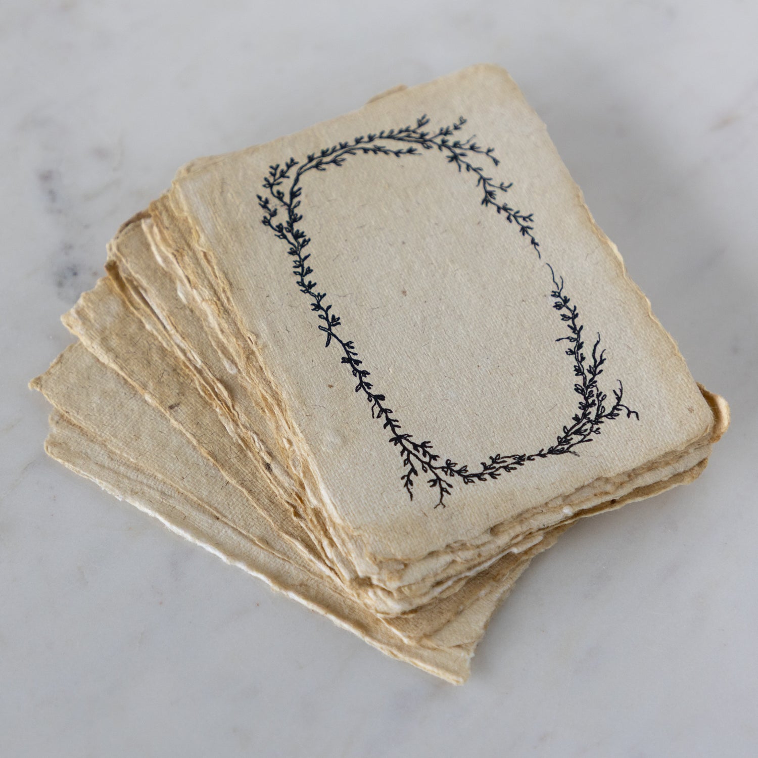 Stack of vintage-style cards with decorative leaf design on a marble surface.