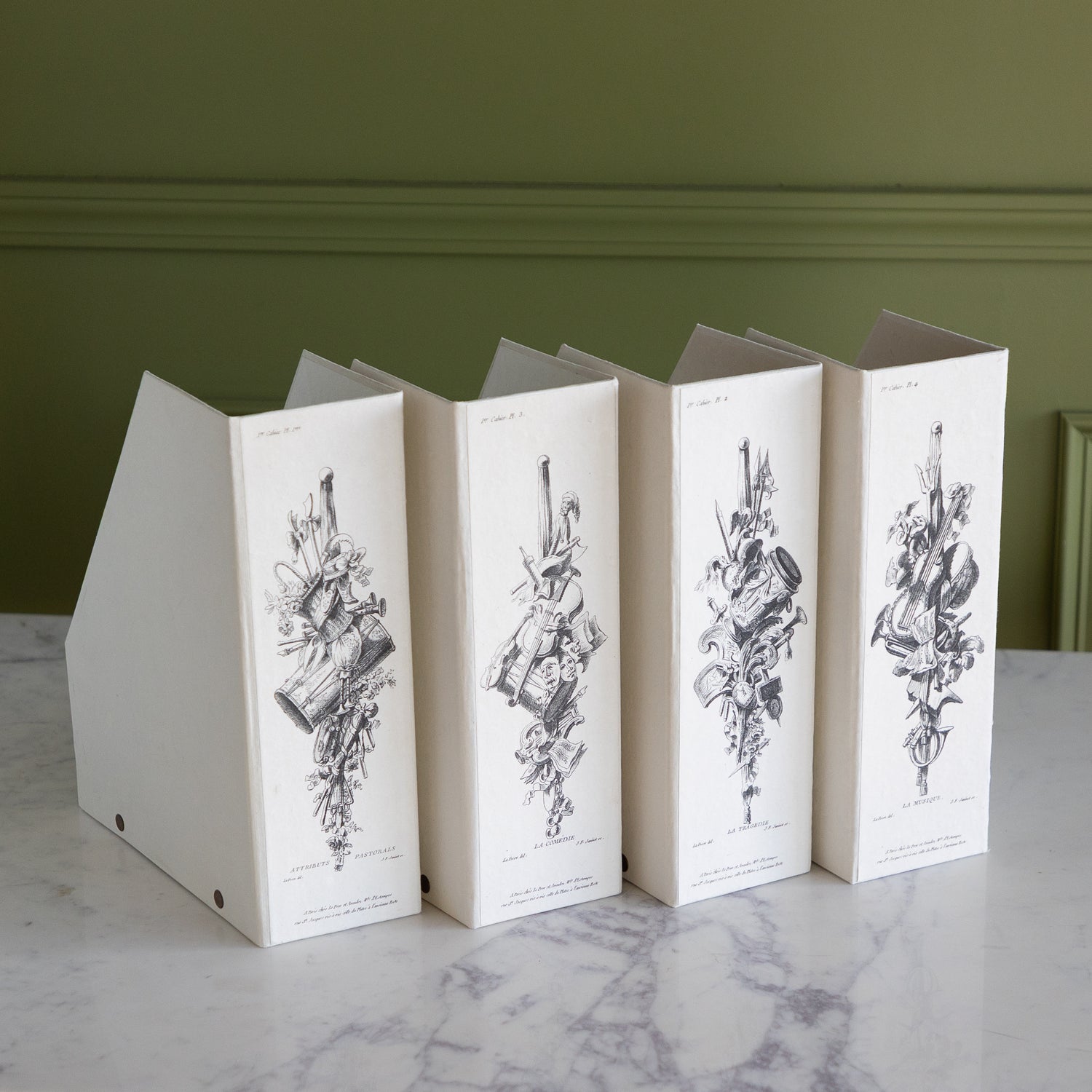 Four folding file boxes with decorative illustrations on a marble table against a green wall.