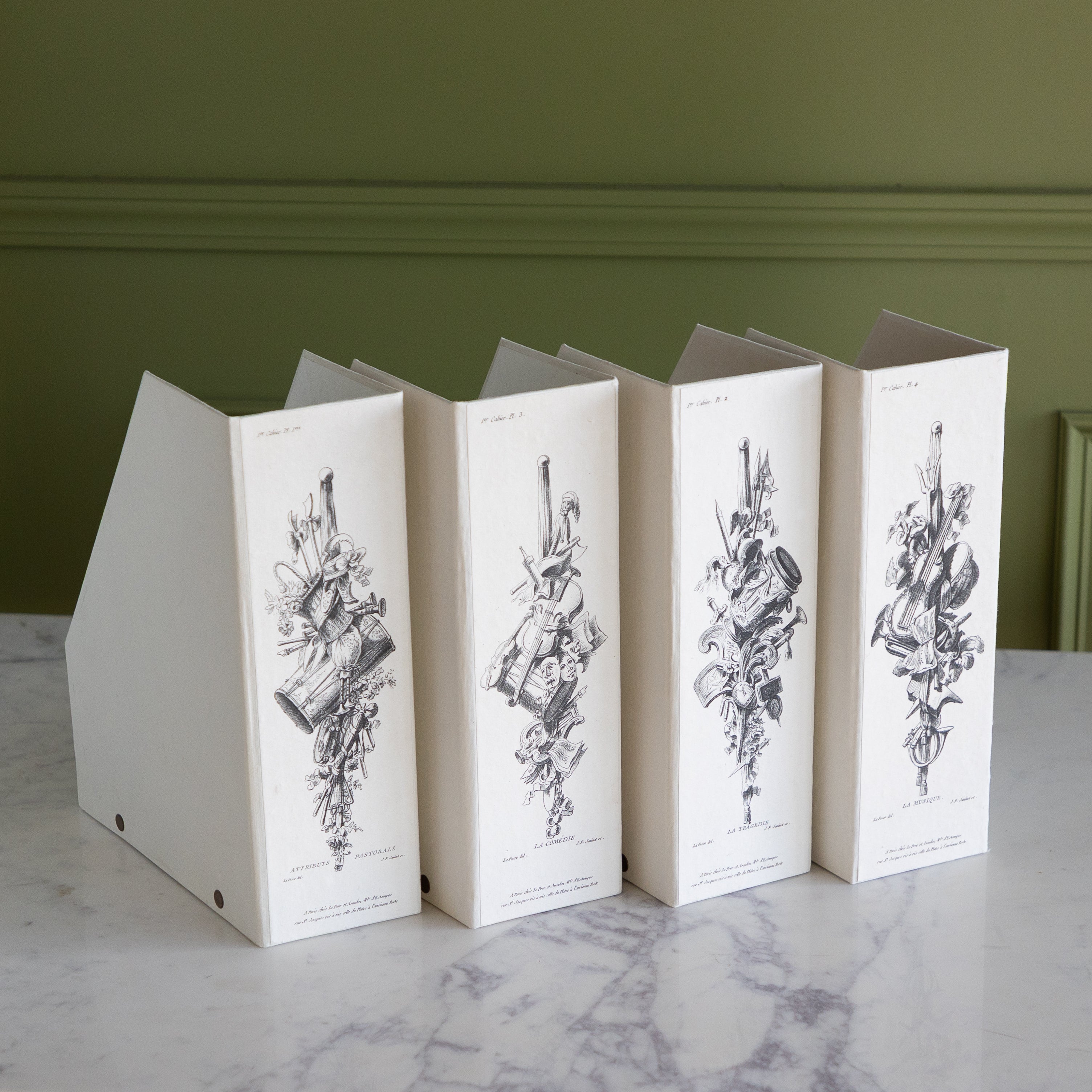 Four folding file boxes with decorative illustrations on a marble table against a green wall.