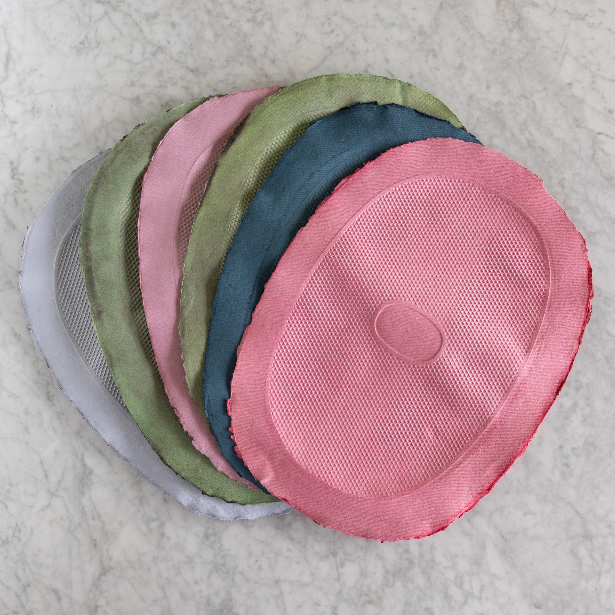 Stack of Multicolored Paper Placemats fanned out on a marble table.