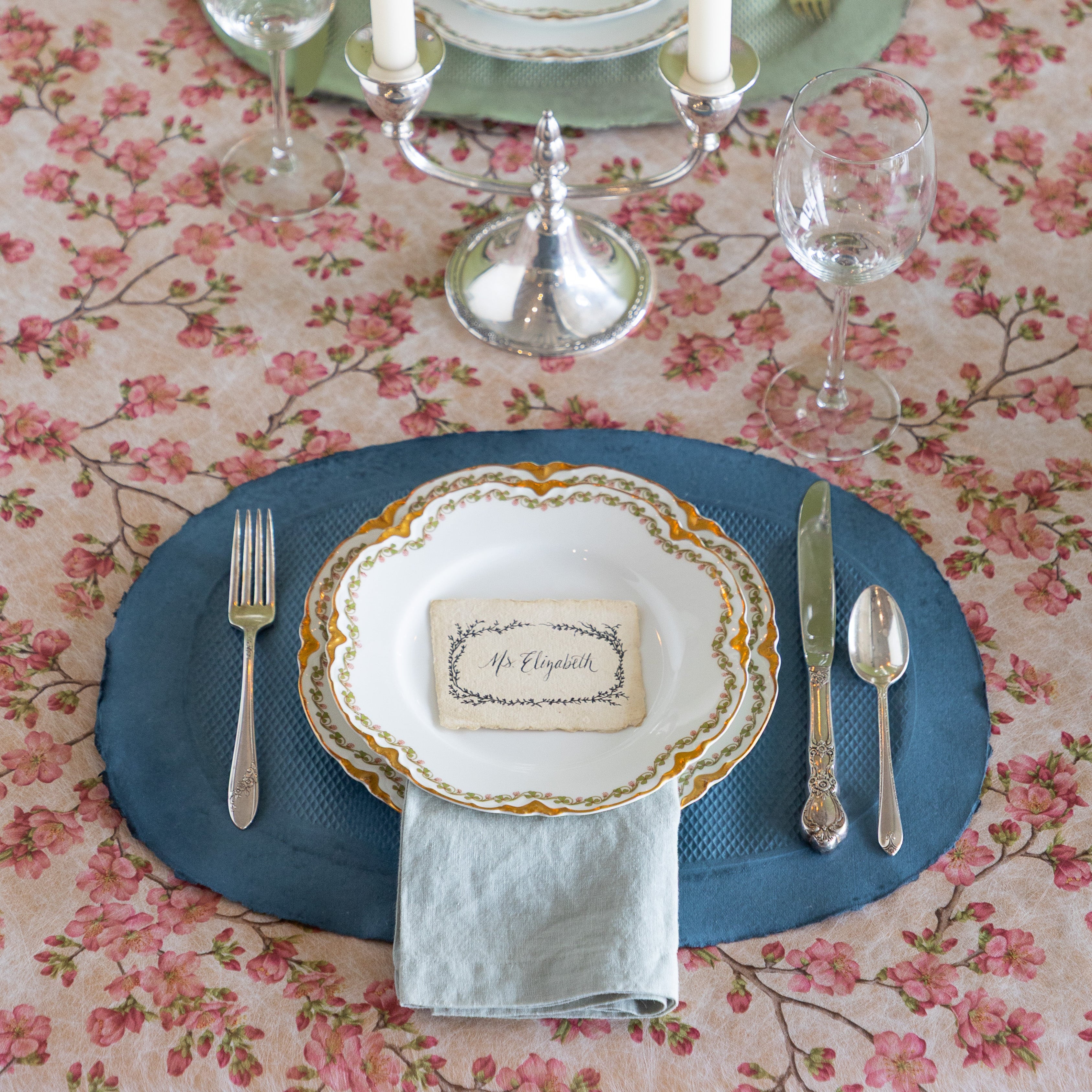 Elegant table setting with a blue paper placemat, candles, and silverware on the Pink Cherry Blossom Runner.