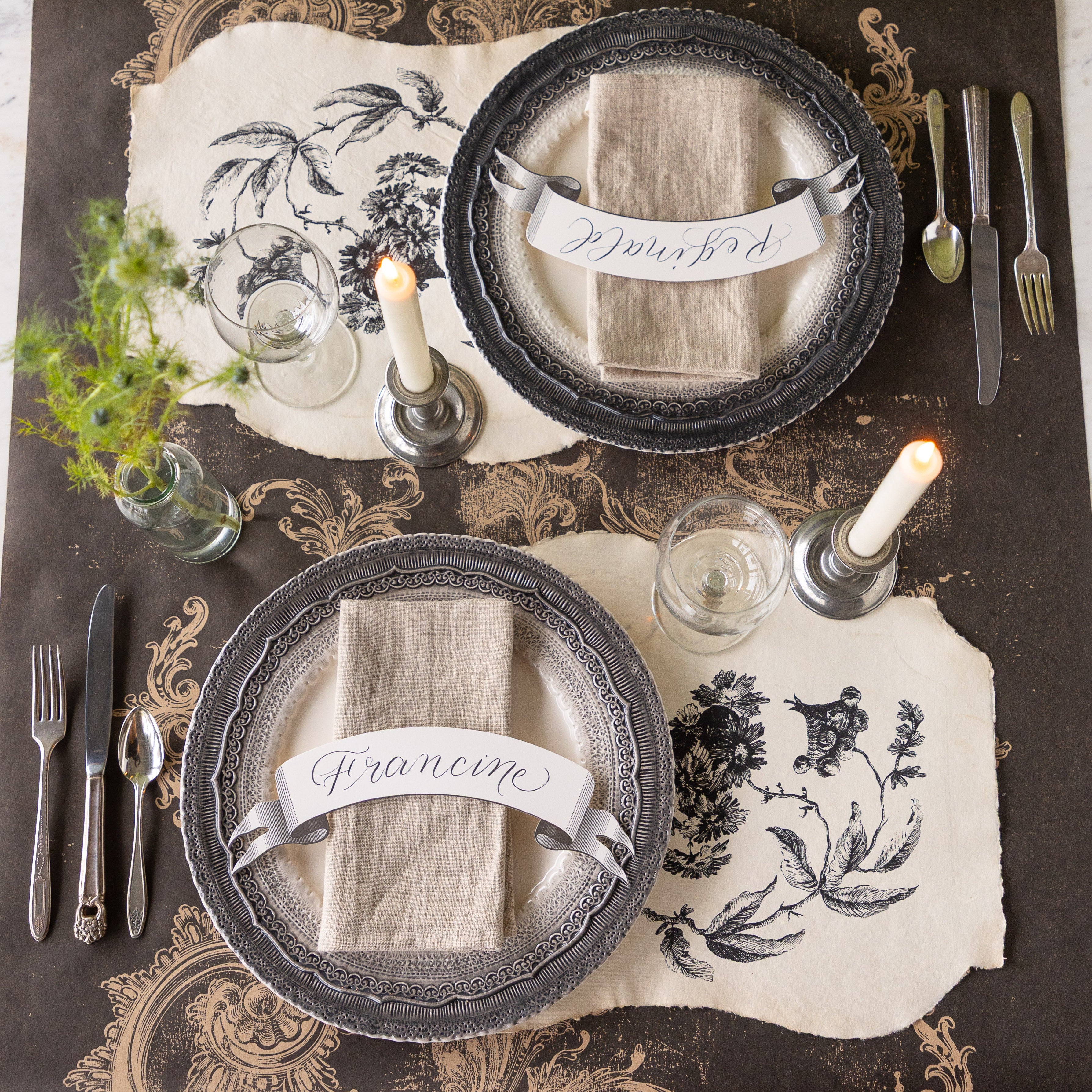Table setting with decorative plates, Pillement Paper Placemats, glasses, and candles on the Black Archival Runner.