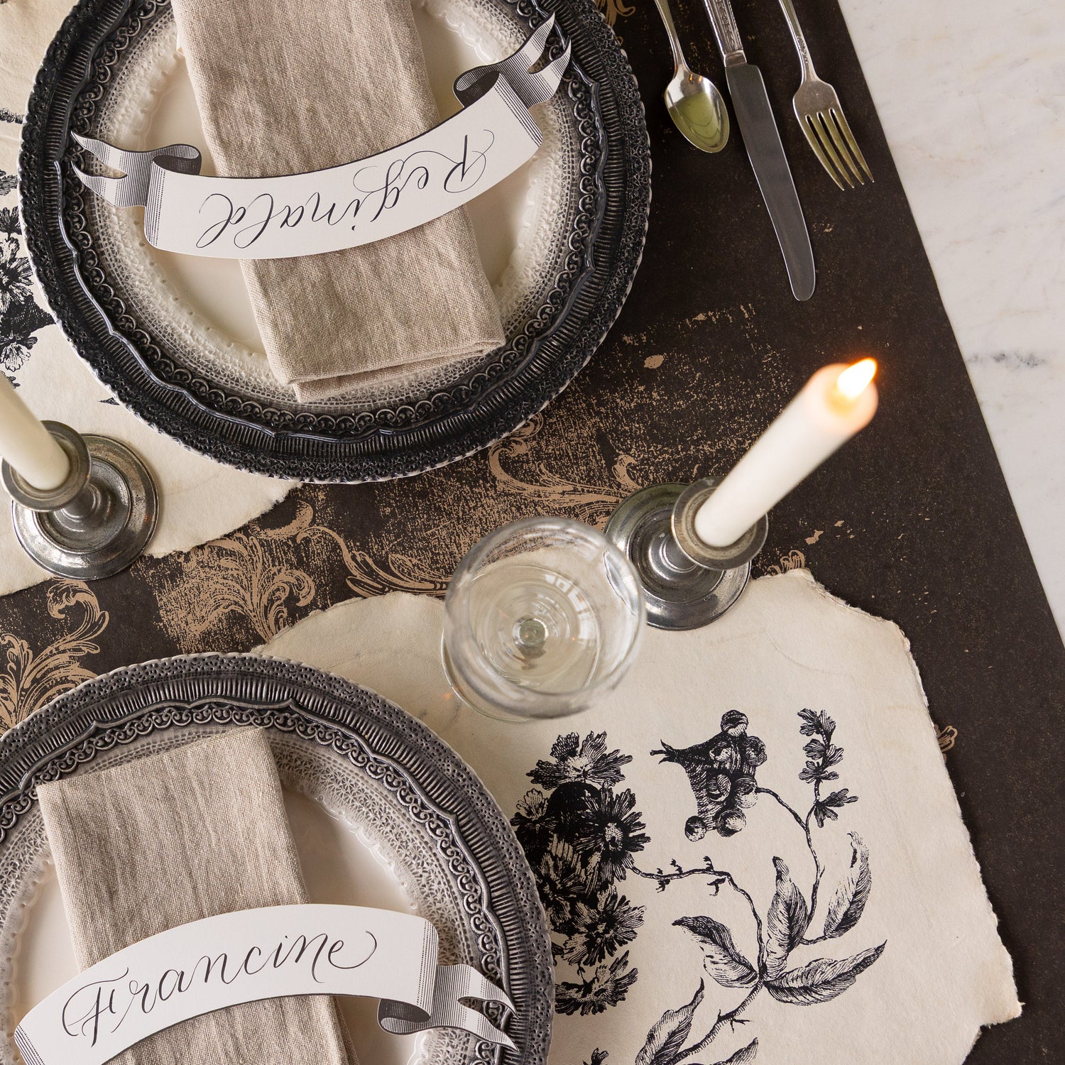 Elegant place setting with decorative plates, Pillement Paper Placemats, Classic Banner Table Accent, glasses, and candles on the Black Archival Runner.