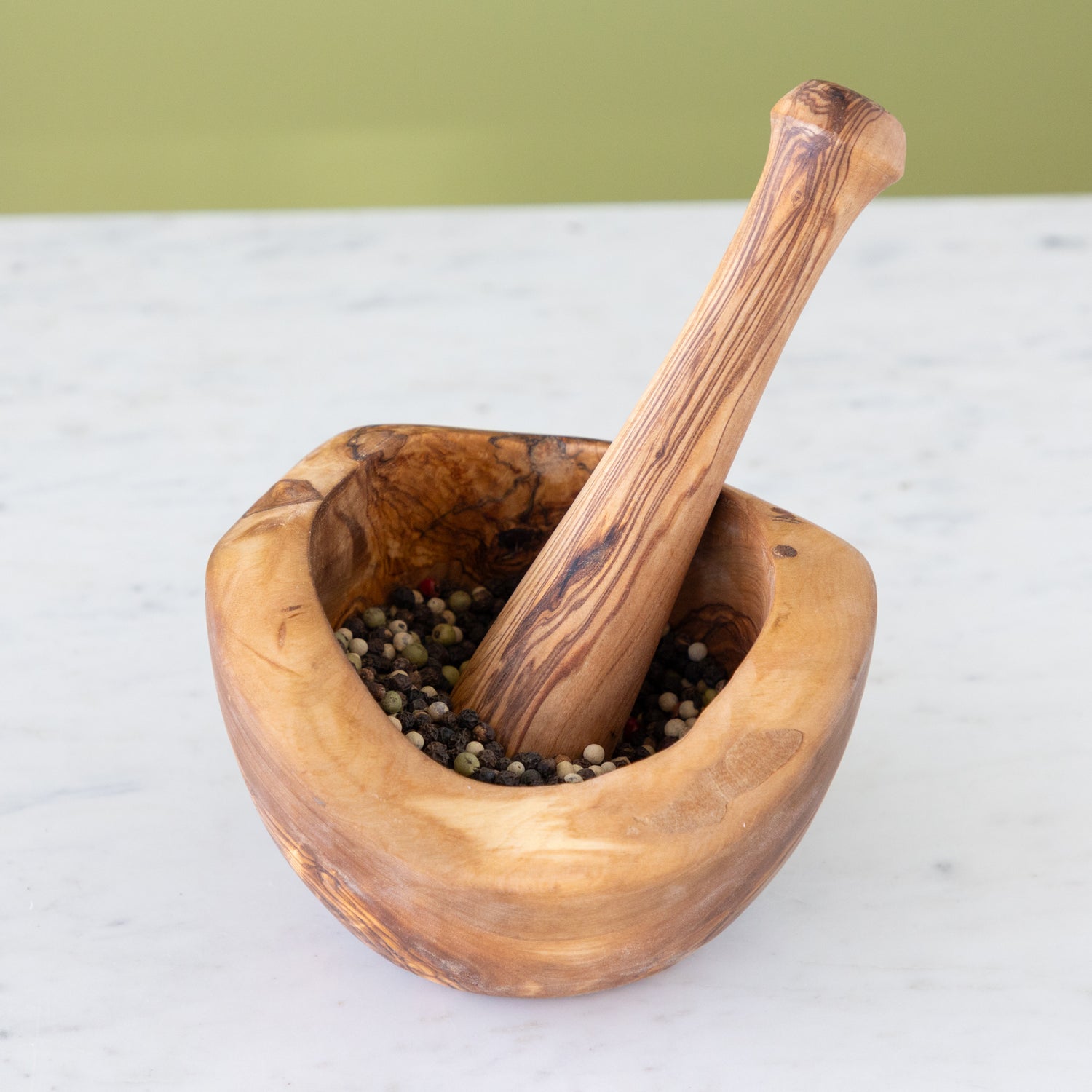 Wooden mortar and pestle with peppercorns on a white surface.