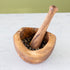 Wooden mortar and pestle with peppercorns on a white surface.