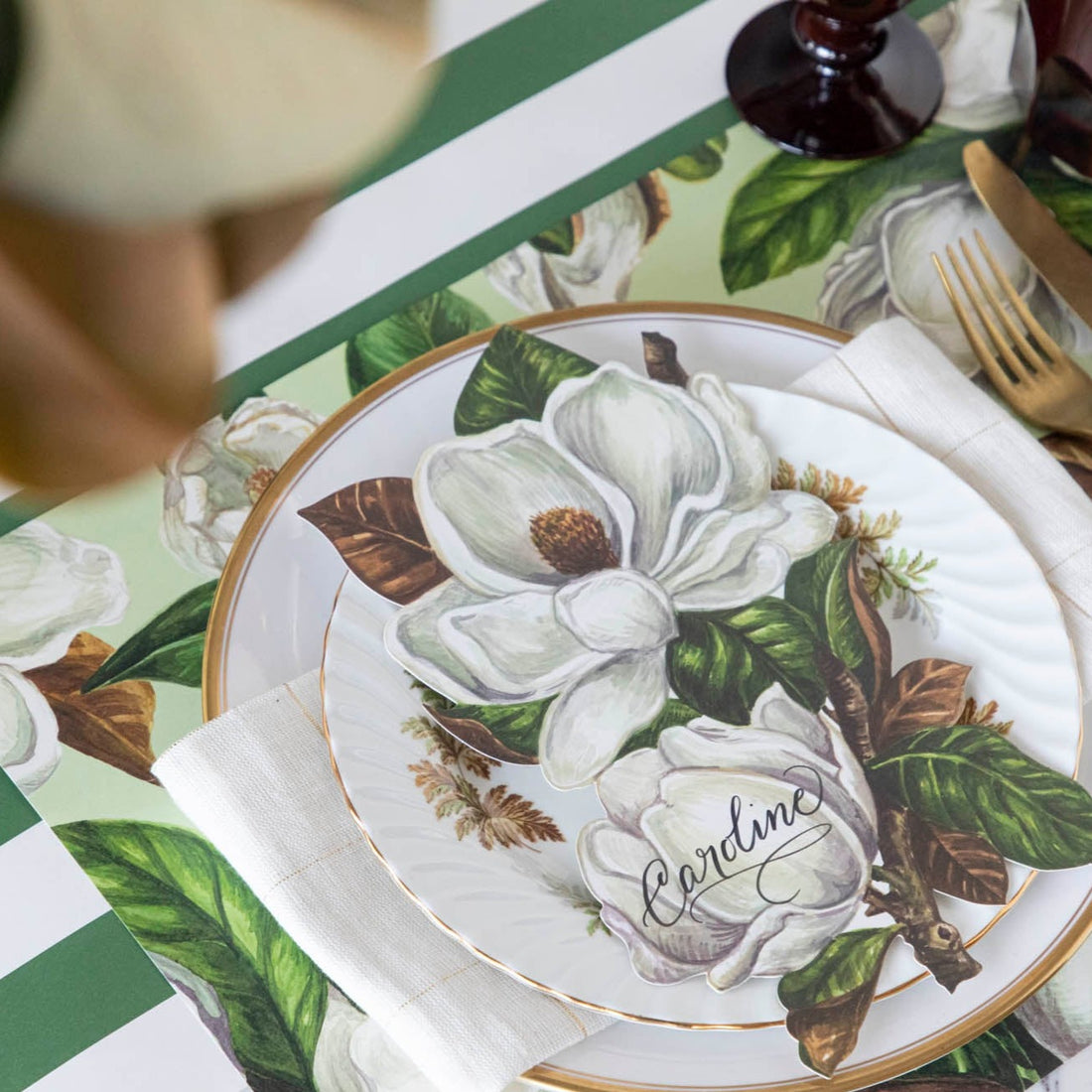 An elegant place setting featuring a Magnolia Blooms Table Accent with &quot;Caroline&quot; written in beautiful script resting on the plate.