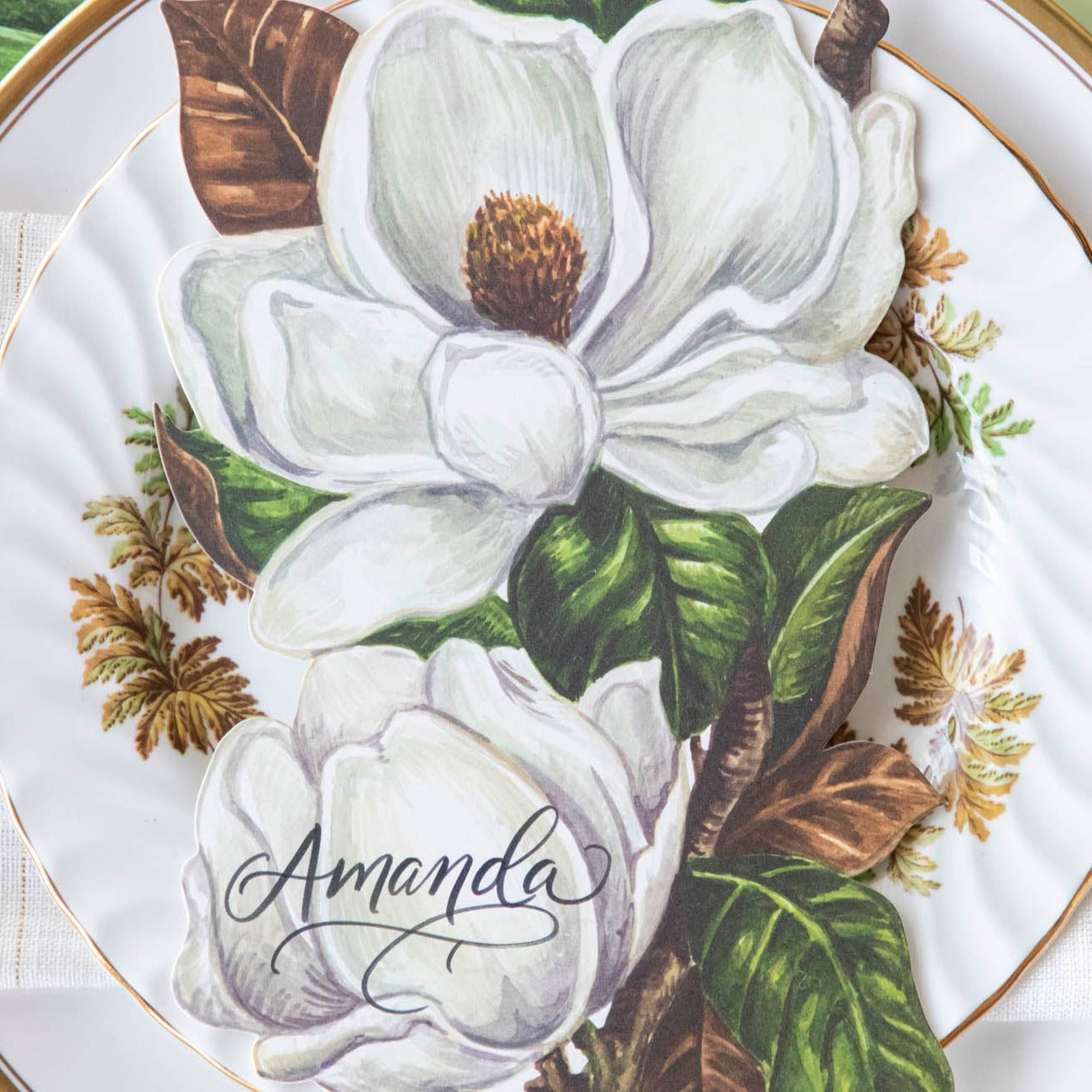 Close-up of an elegant place setting featuring a Magnolia Blooms Table Accent with &quot;Amanda&quot; written in beautiful script resting on the plate.