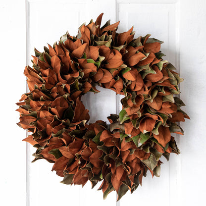 A one week old magnolia wreath hanging on a door.