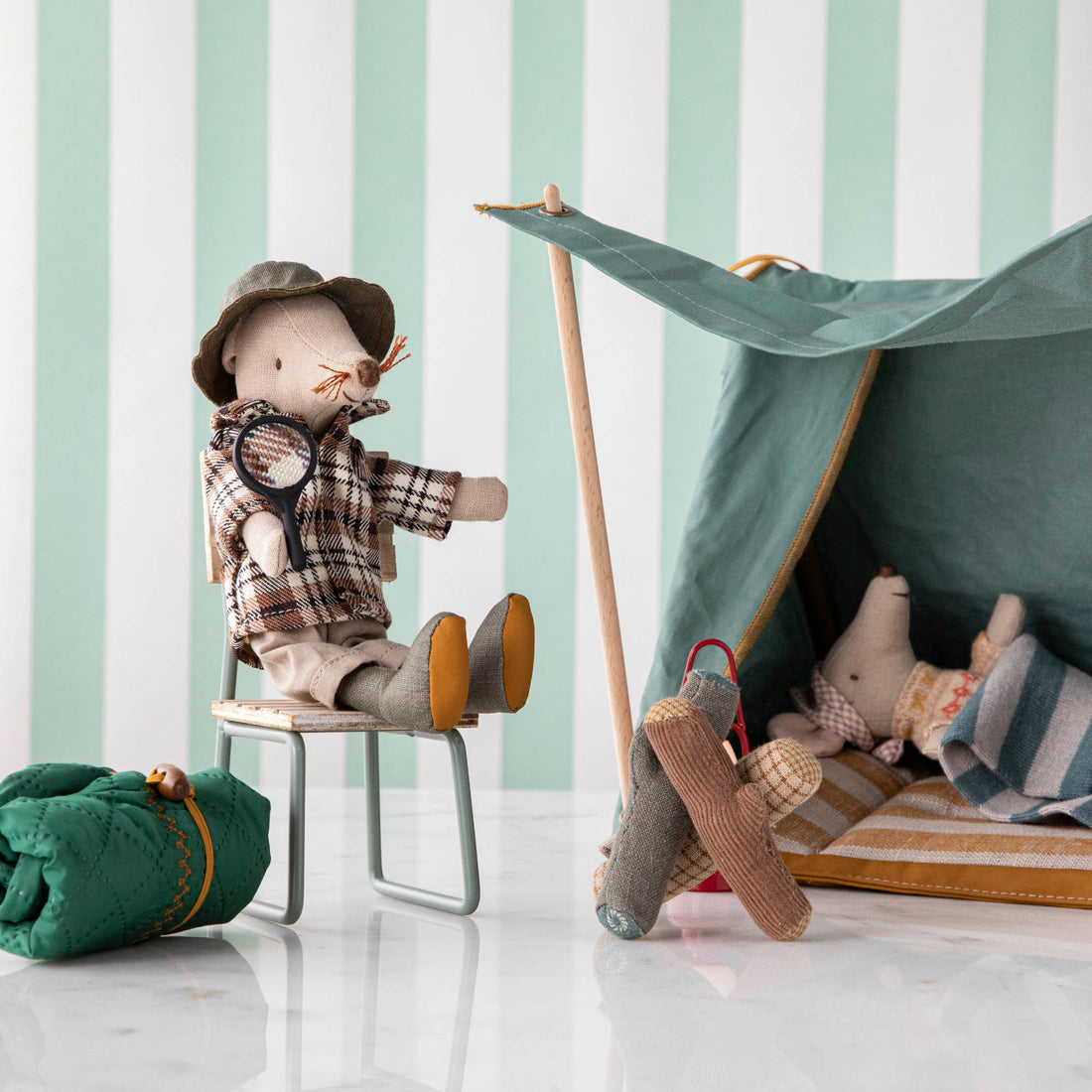 A Maileg Wildlife Guide Mouse sitting on a chair next to a tent during a hiking trip.